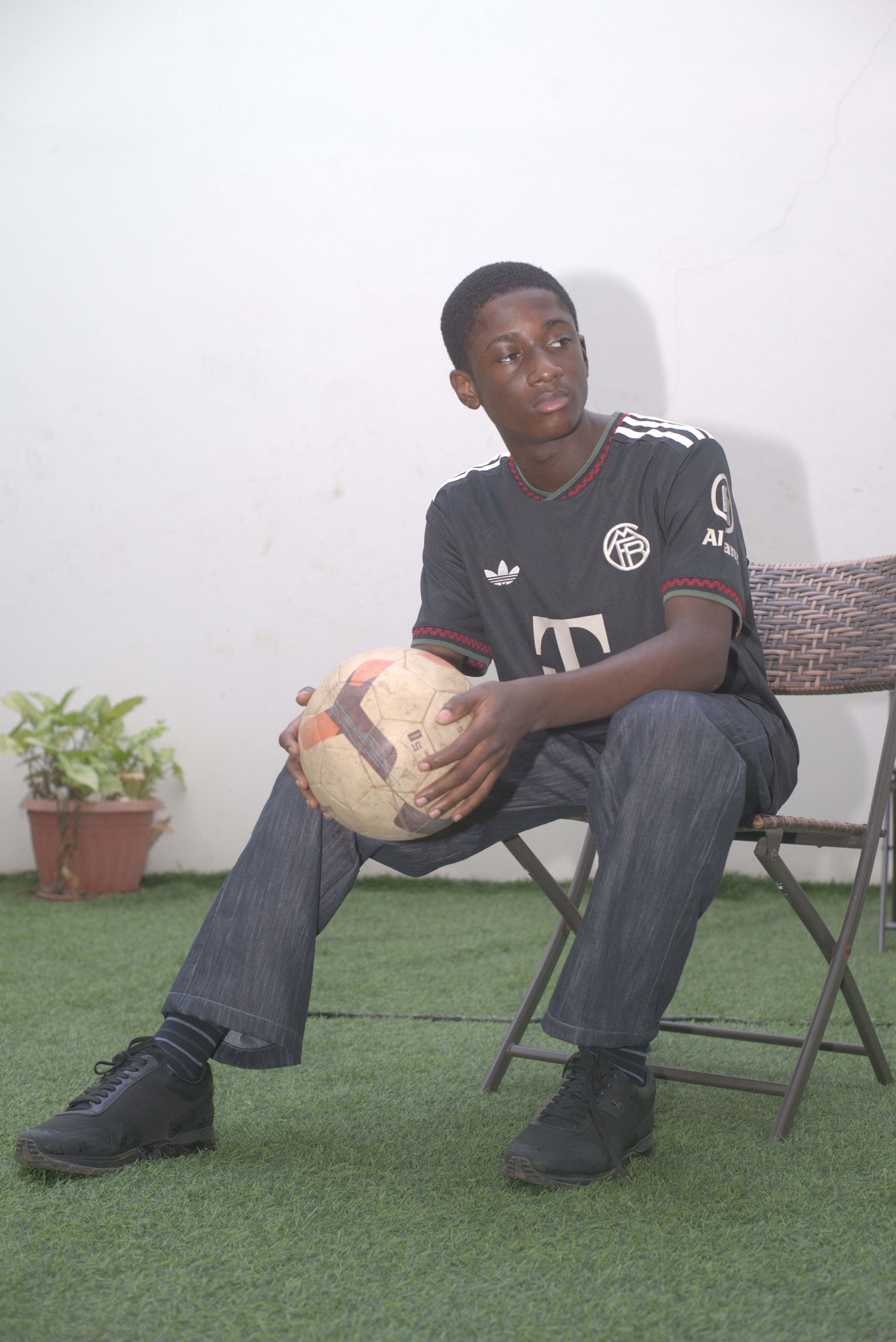 Teenage boy seated outdoors holding a soccer ball, with a calm expression.