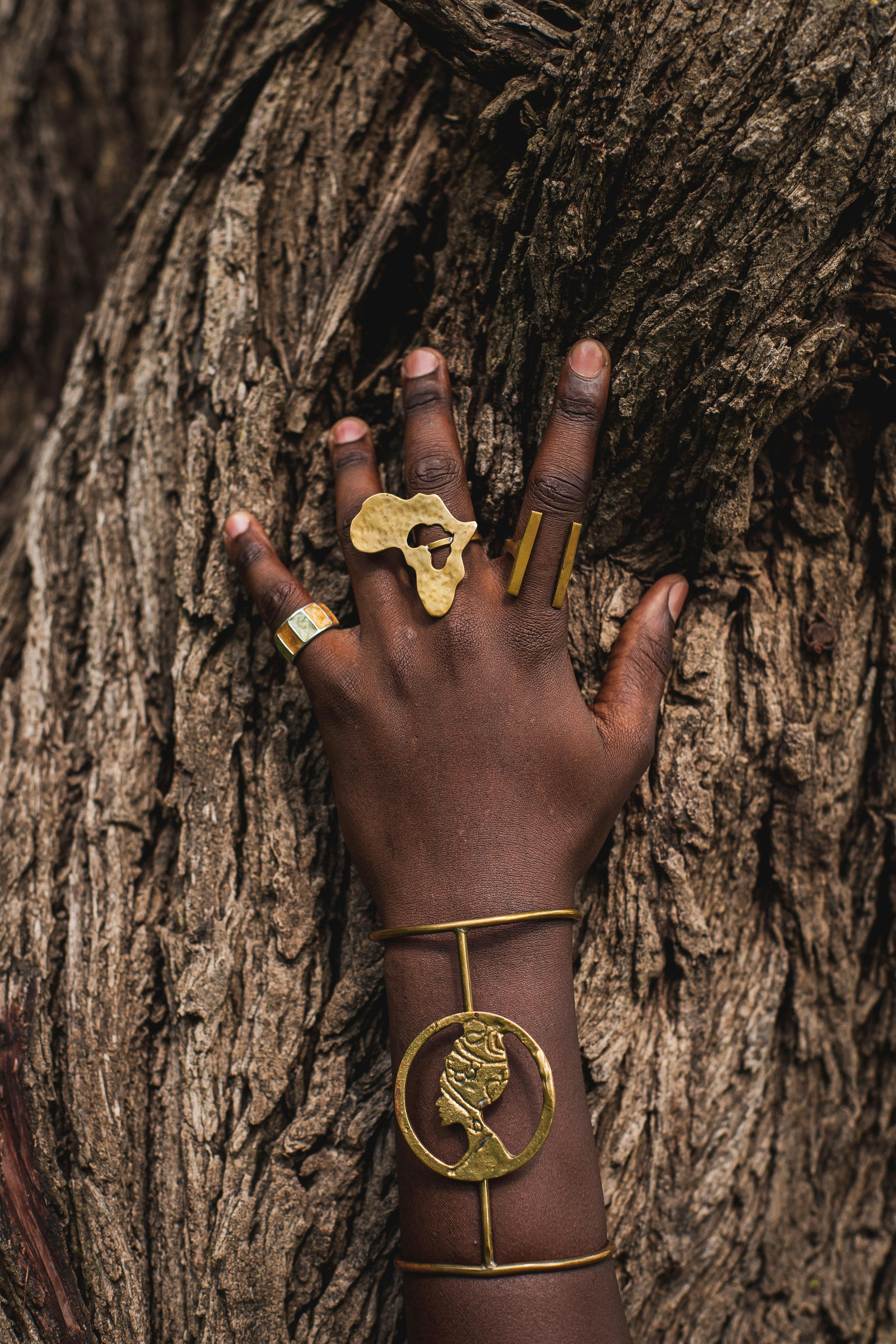 Gratuit O mână împodobită cu bijuterii din aur de inspirație africană, așezate pe o scoarță texturată de copac, etalând eleganță culturală. Fotografie de stoc