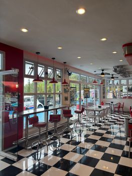Empty retro American diner with checkered floor, vintage cars, and red accents.