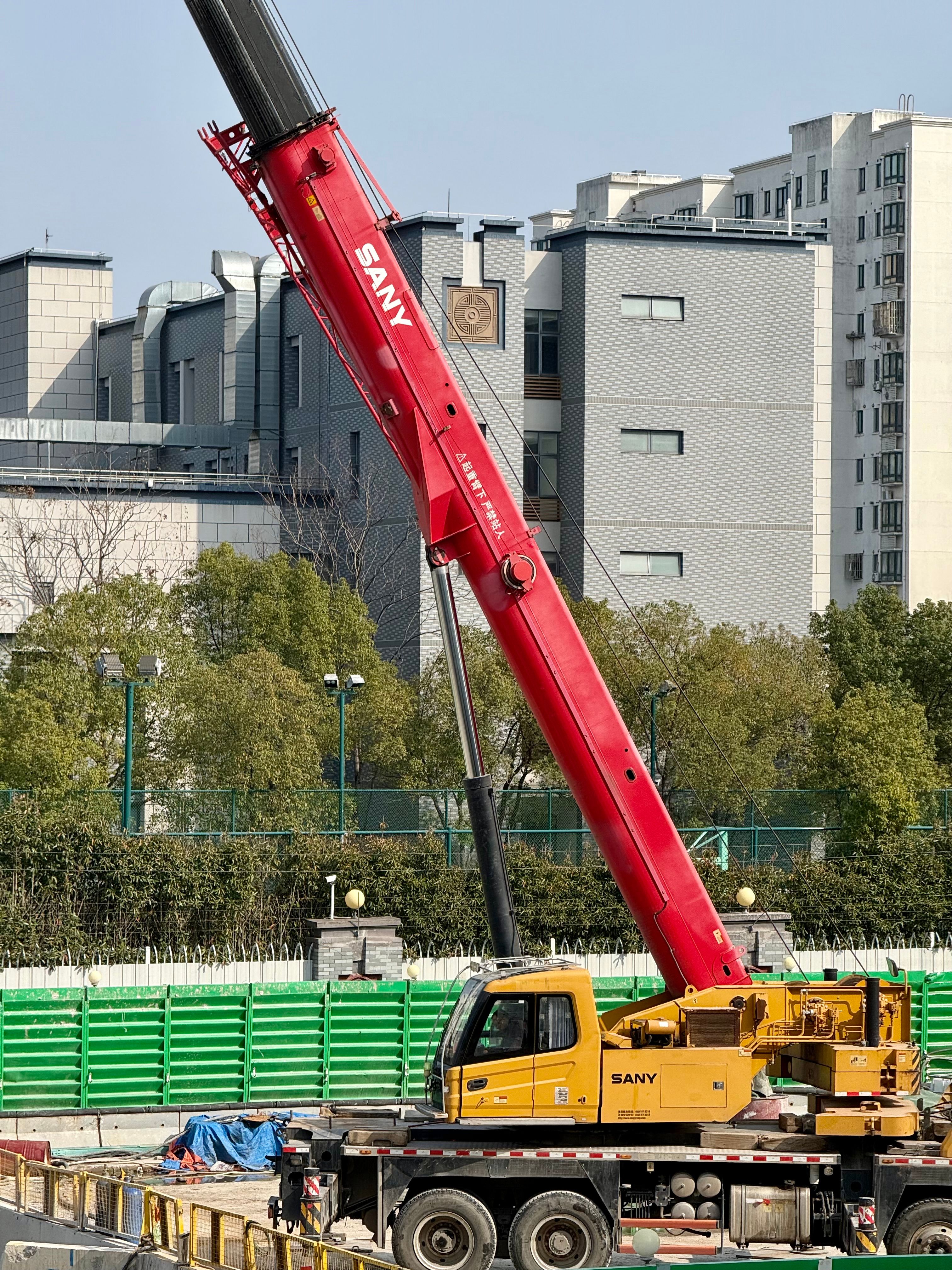 Red SANY crane at a construction site in Shanghai on a clear day, showcasing urban development.