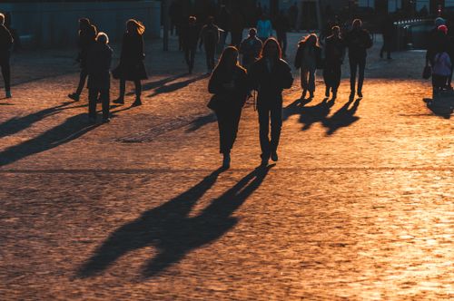 Free A diverse group of silhouettes walks on sunlit cobblestones, casting long shadows in the golden hour. Stock Photo