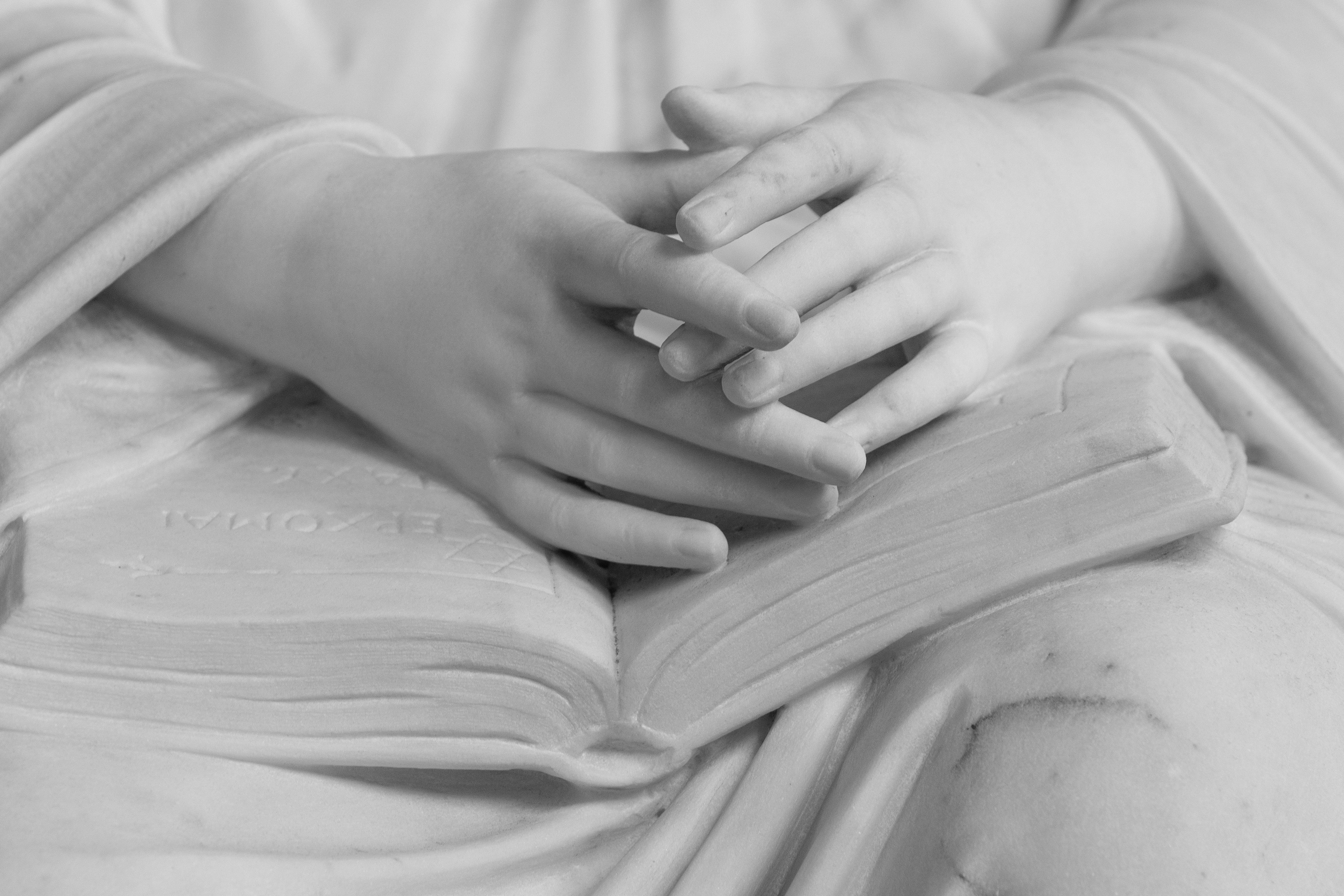 Gratis Dettaglio in bianco e nero, primo piano di mani su una scultura in pietra raffigurante una Bibbia, simbolo di fede. Foto a disposizione