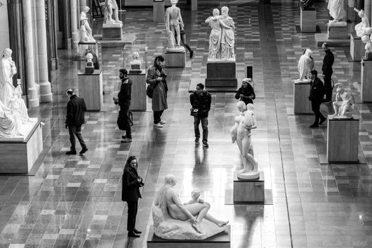 Visitors explore a museum gallery filled with classical sculptures.