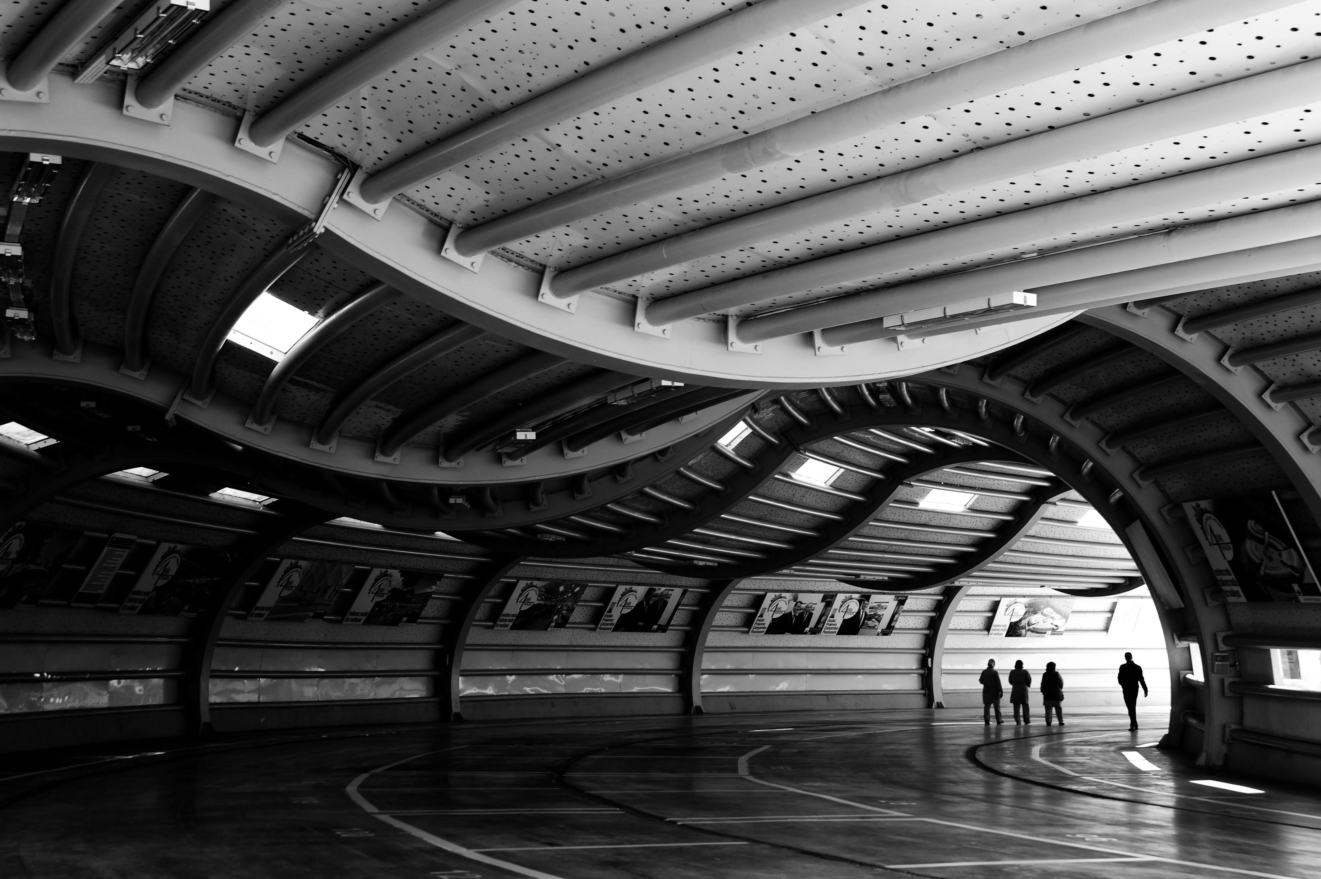 無料 光を背景に人物のシルエットが浮かび上がる、建築的なトンネルを写した白黒写真。 写真素材