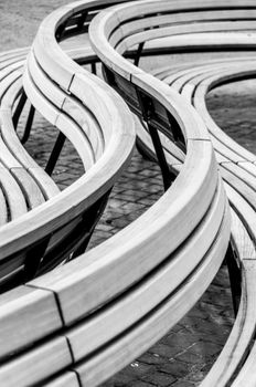 Abstract black and white photo of modern curved wooden benches on cobblestone pavement.