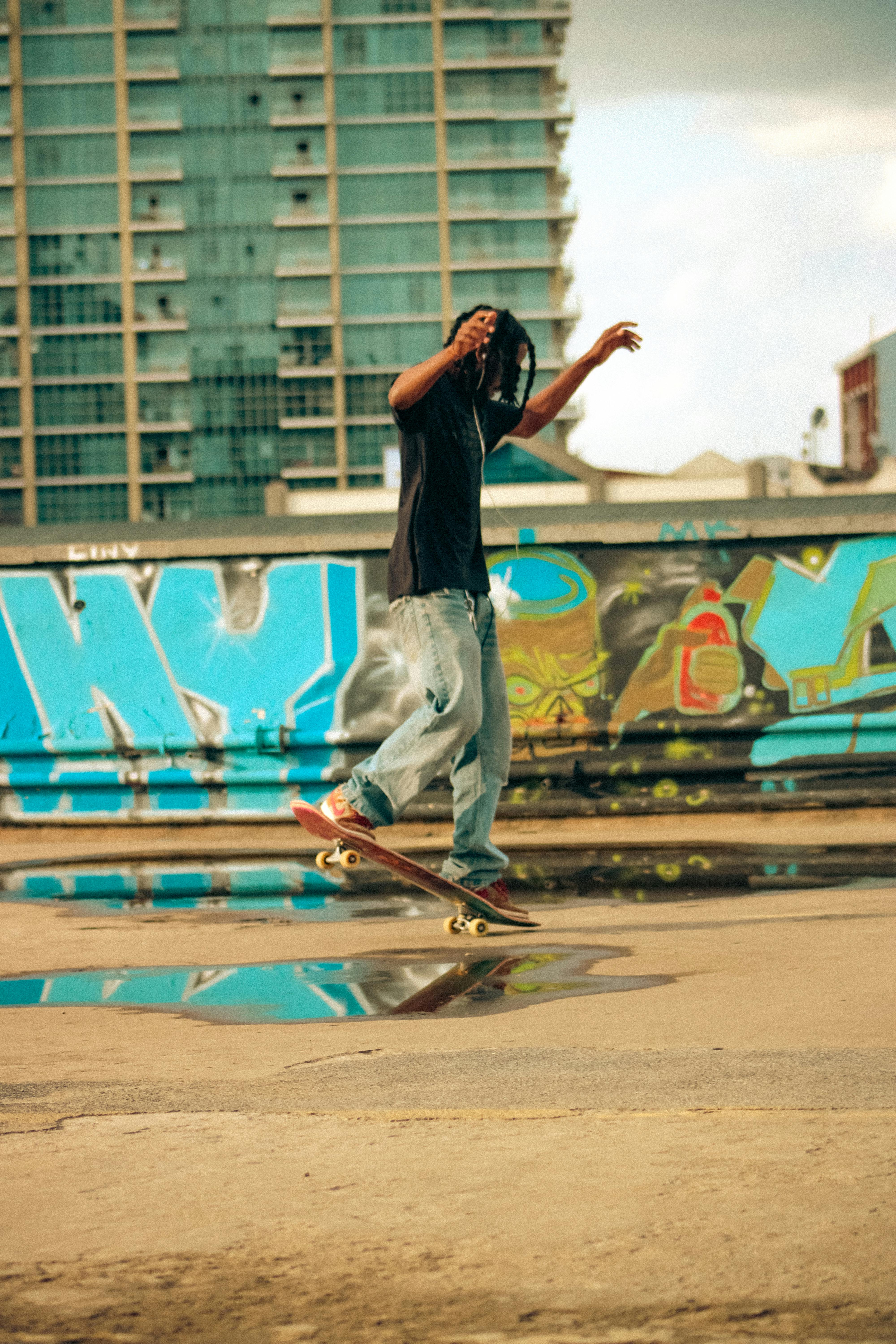 Gratis Giovane skater che esegue acrobazie davanti a uno sfondo di graffiti colorati. Atmosfera urbana ed energica. Foto a disposizione