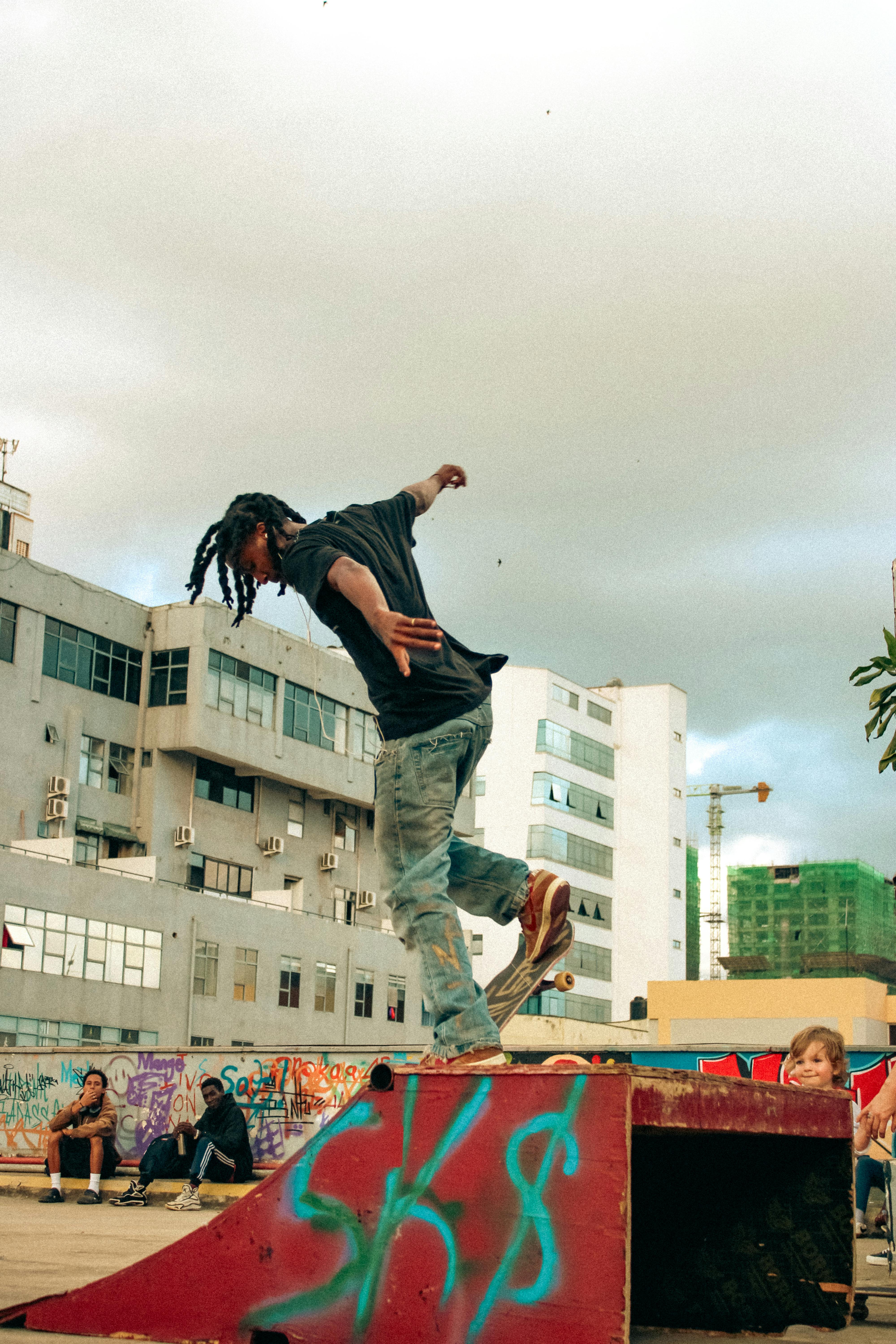 Kostenlos Ein Skateboarder führt in einem mit Graffiti bedeckten Stadtgebiet einen Trick vor und demonstriert damit die Dynamik der Straßenkultur. Stock-Foto