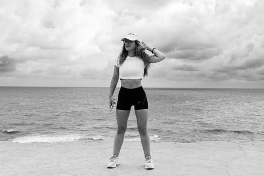 A woman in athletic attire poses near the ocean with a dramatic sky in Natal, Brazil.