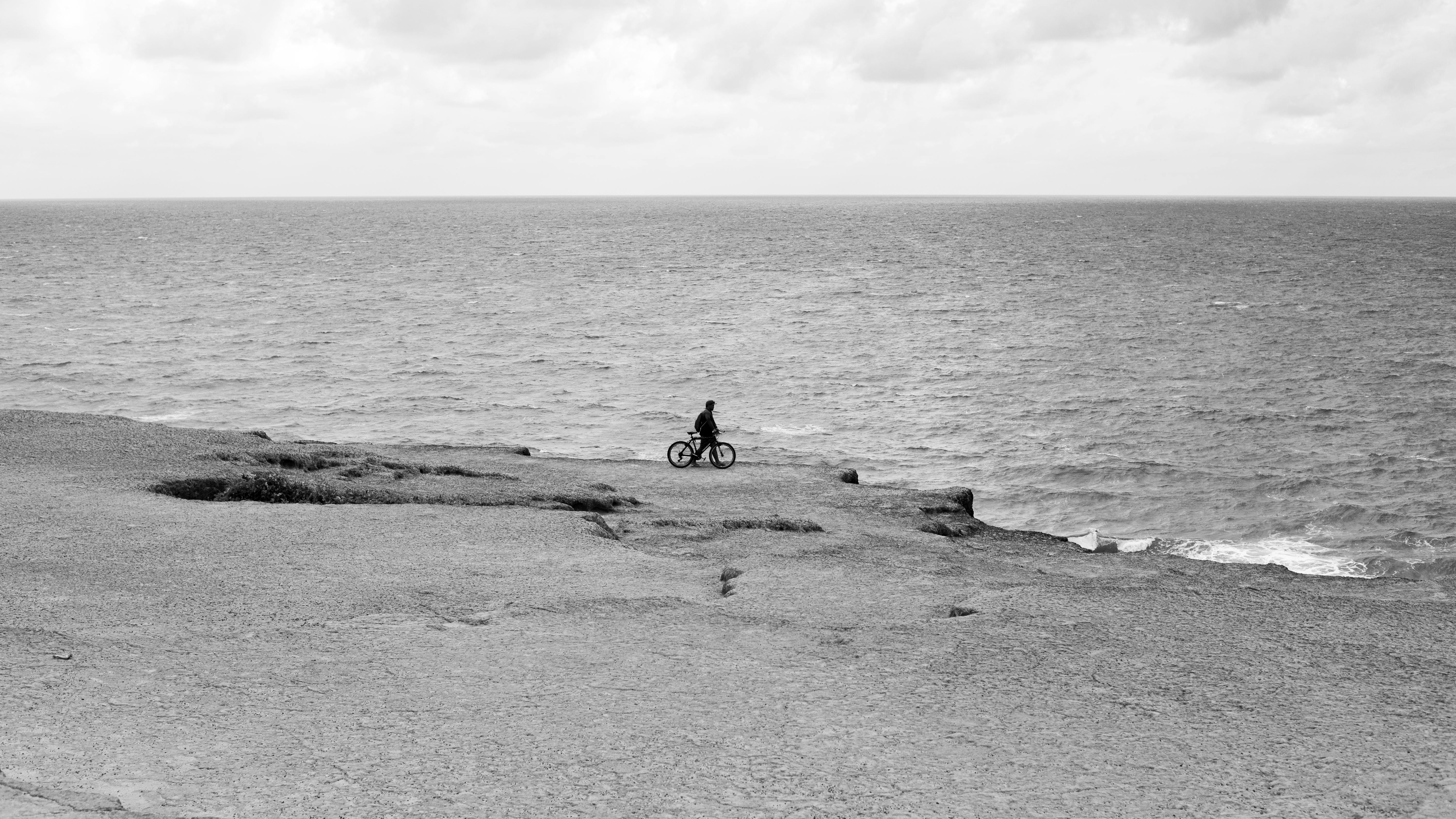 Gratuit Un cycliste roule seul sur un sentier à flanc de falaise, avec l'océan en toile de fond, créant une scène sereine et contemplative. Photos