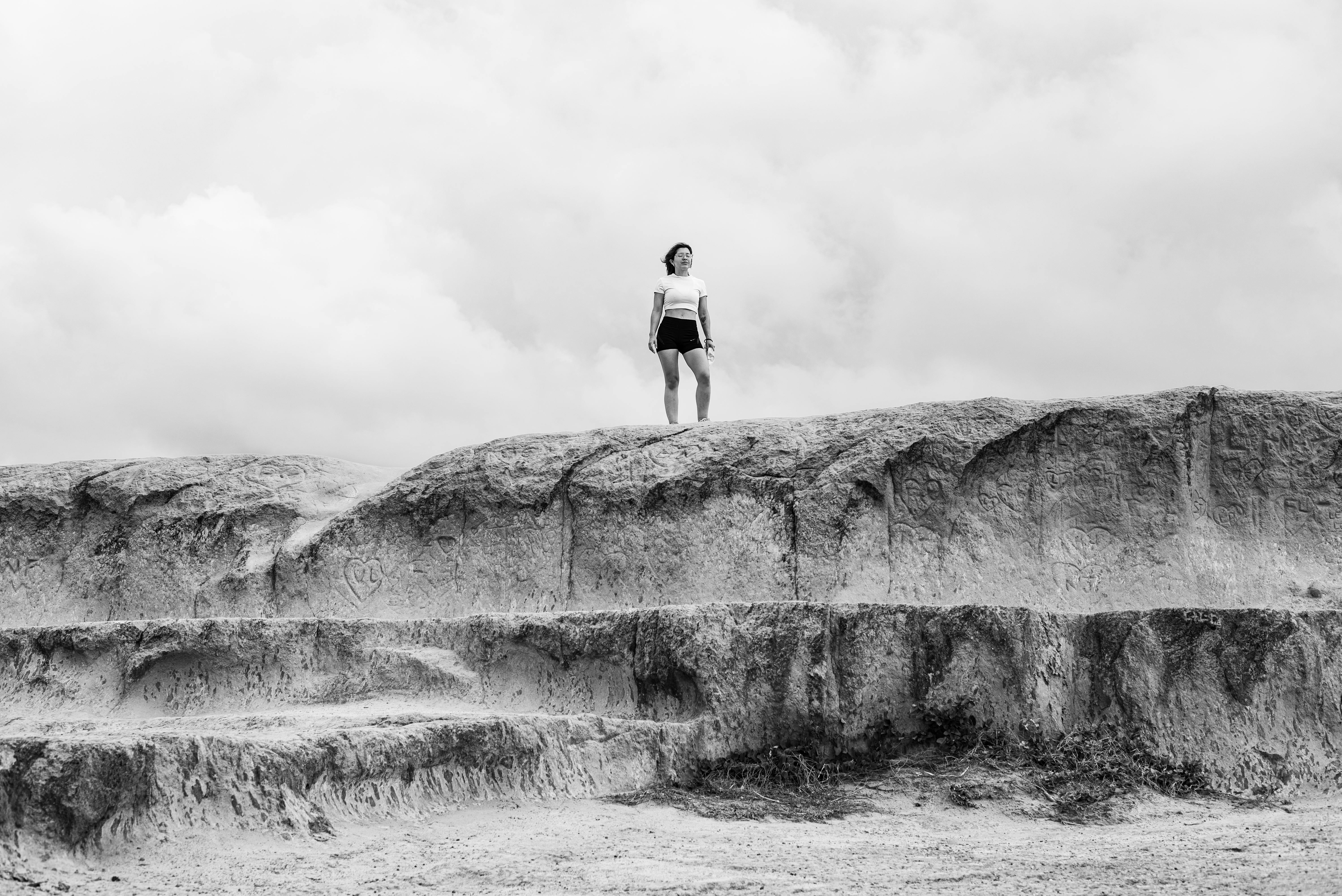 grátis Uma mulher está em pé em um penhasco rochoso sob um céu nublado em Natal, Brasil. Foto profissional