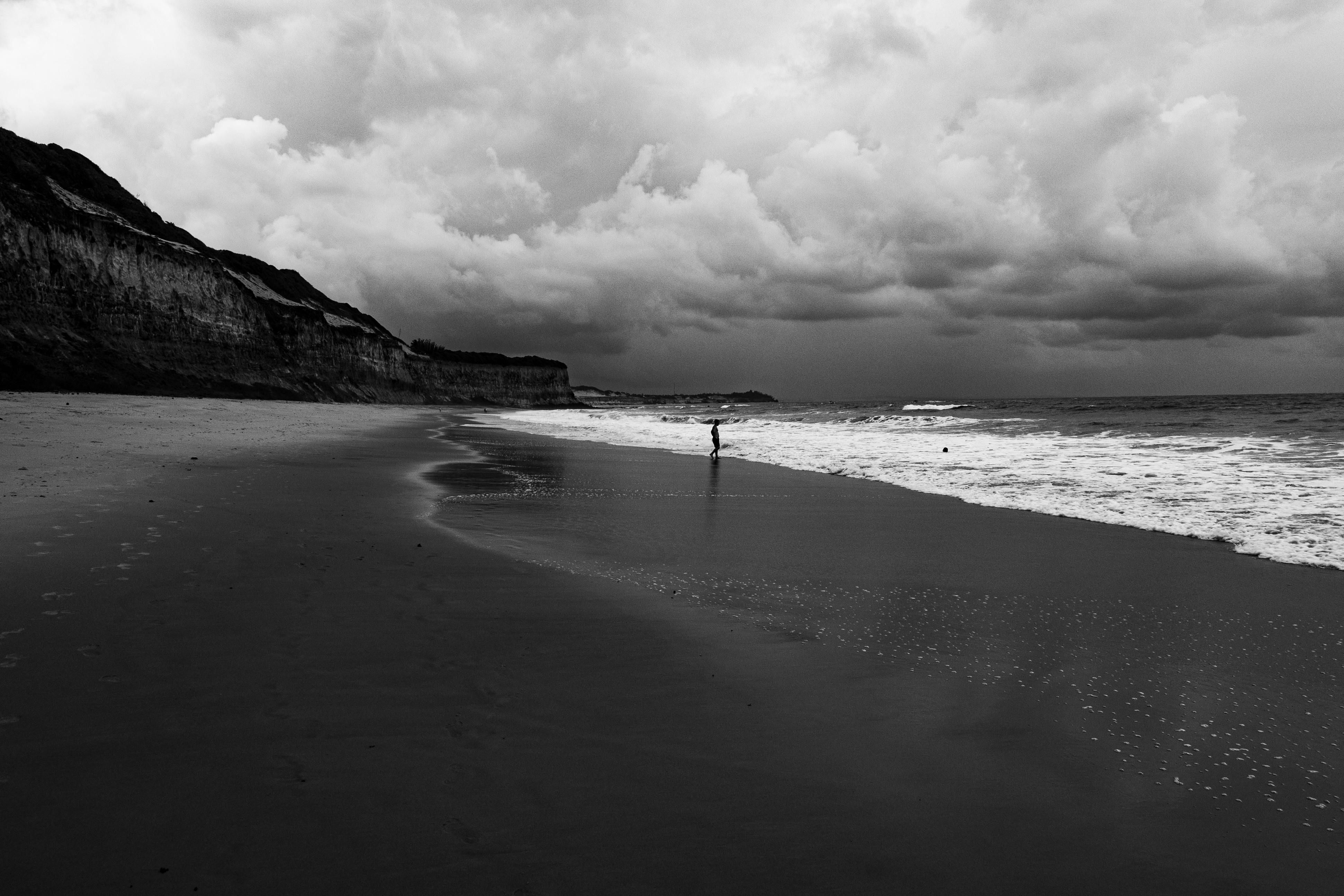 Gratis Scena malinconica in bianco e nero su una spiaggia di Natal, in Brasile, con nuvole suggestive e una figura isolata. Foto a disposizione