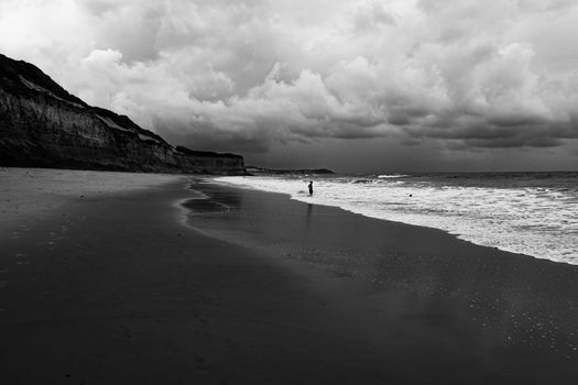 Moody beach landscape with cliffs and ocean waves, captured in black and white.