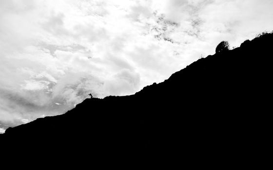 Silhouetted hiker on a steep cliff with dramatic cloudy sky in Natal, Brazil.