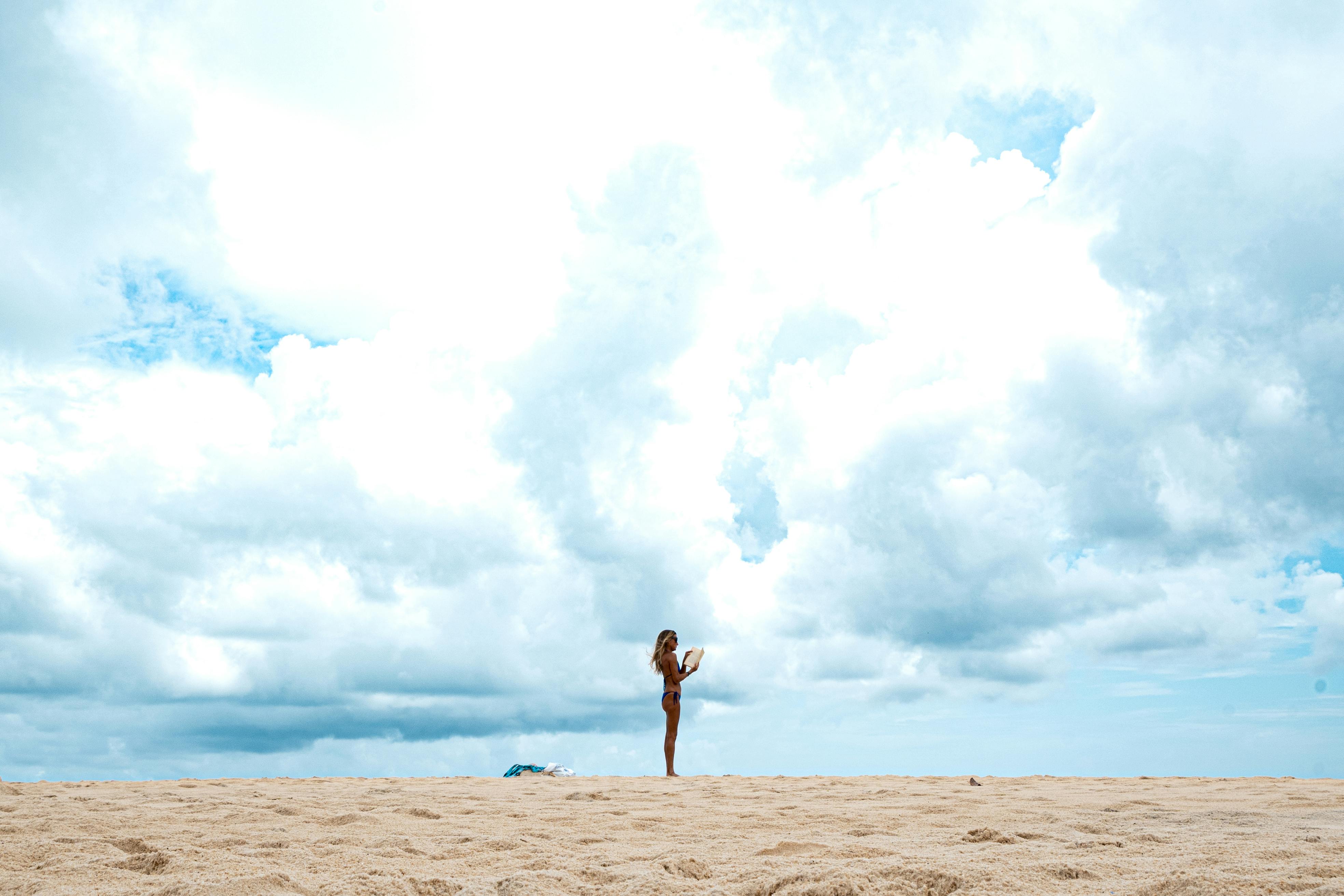 Kostenlos Eine alleinstehende Frau mit Handy unter einem weiten, bewölkten Himmel an einem Strand in Natal, Brasilien. Stock-Foto