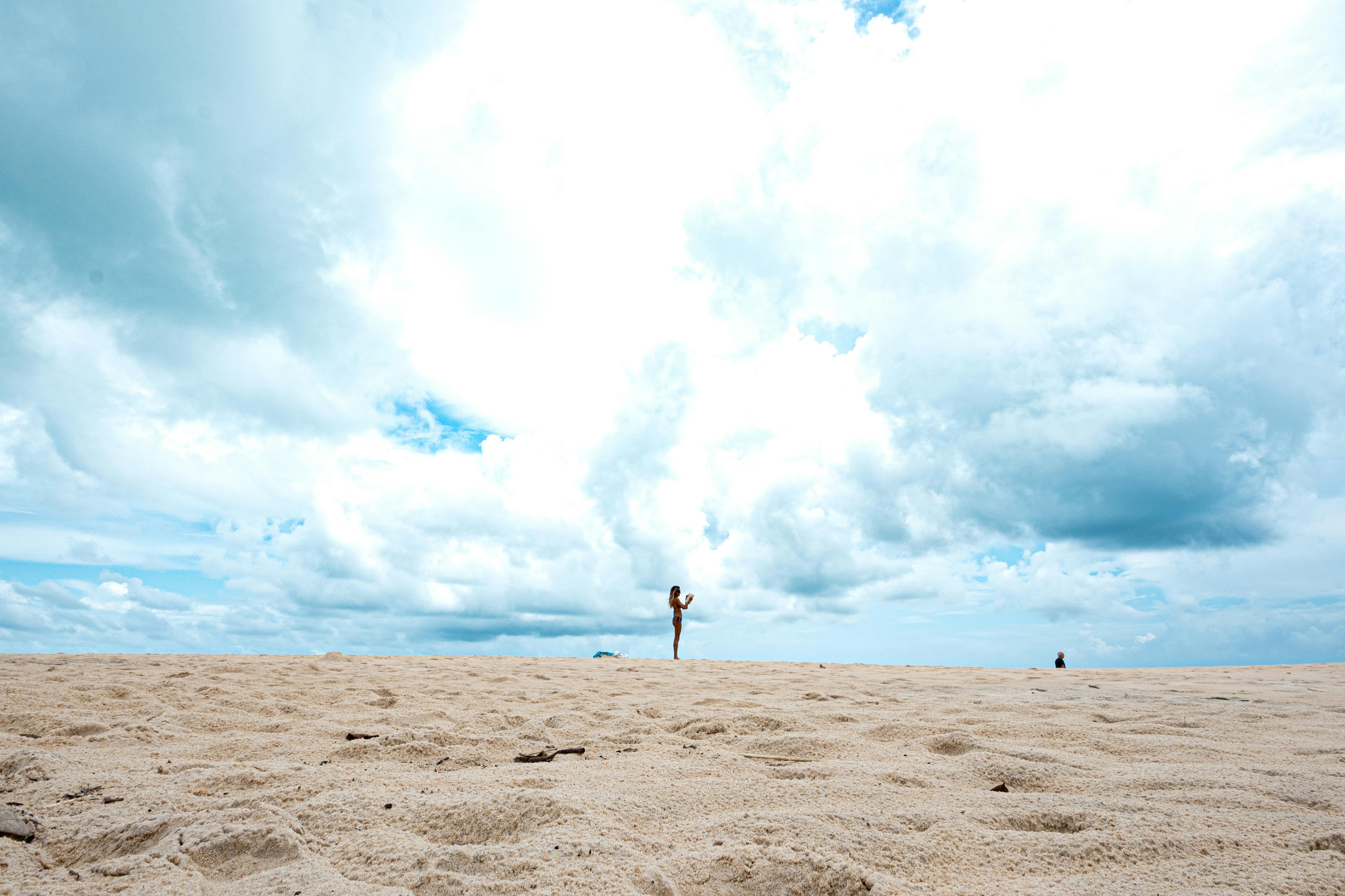 Gratis Una persona cammina su una spiaggia sabbiosa sotto un vasto cielo nuvoloso a Natal, in Brasile. Foto a disposizione