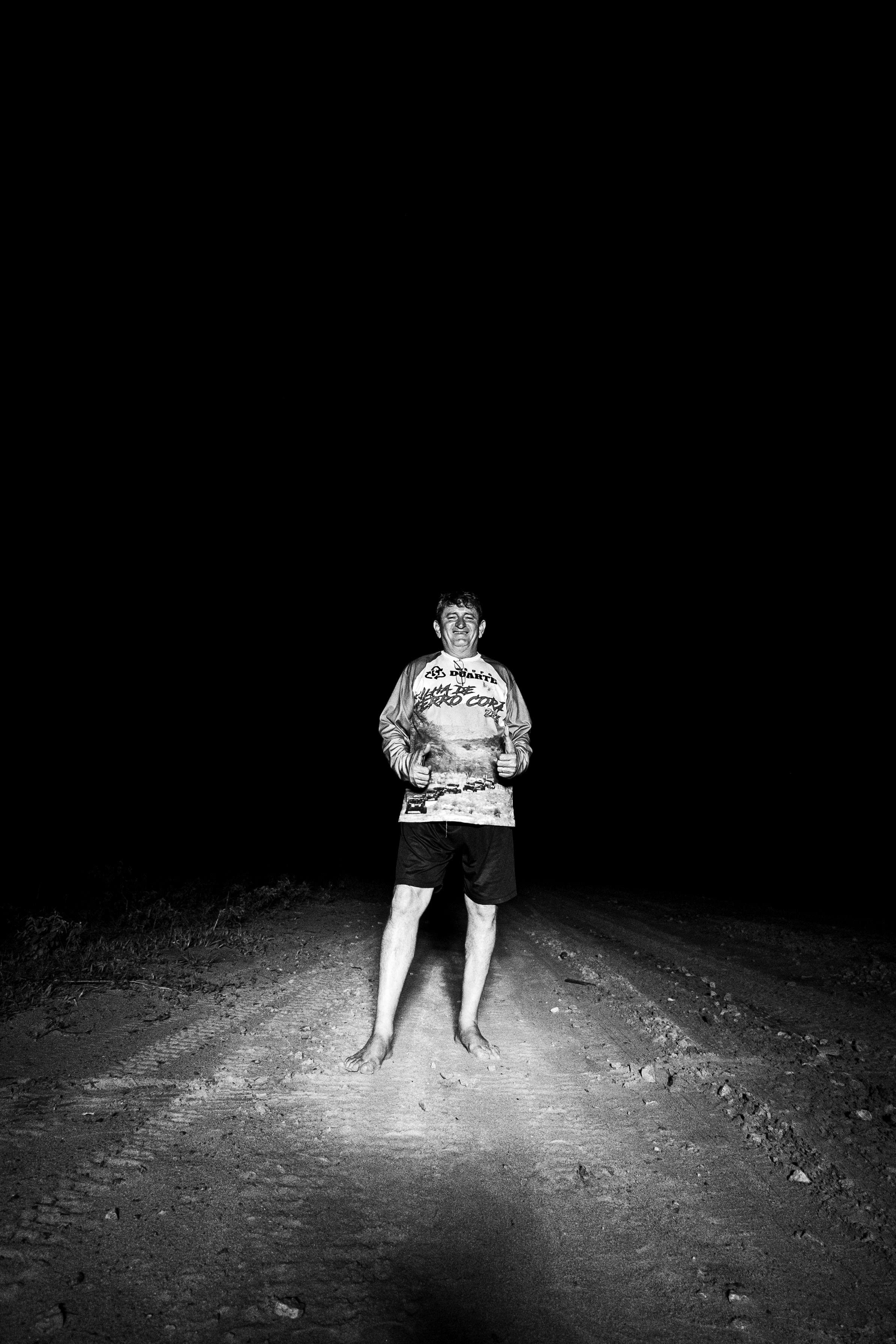 Gratis Una persona solitaria è in piedi, illuminata, su una strada sterrata, immortalata in un crudo bianco e nero. Foto a disposizione