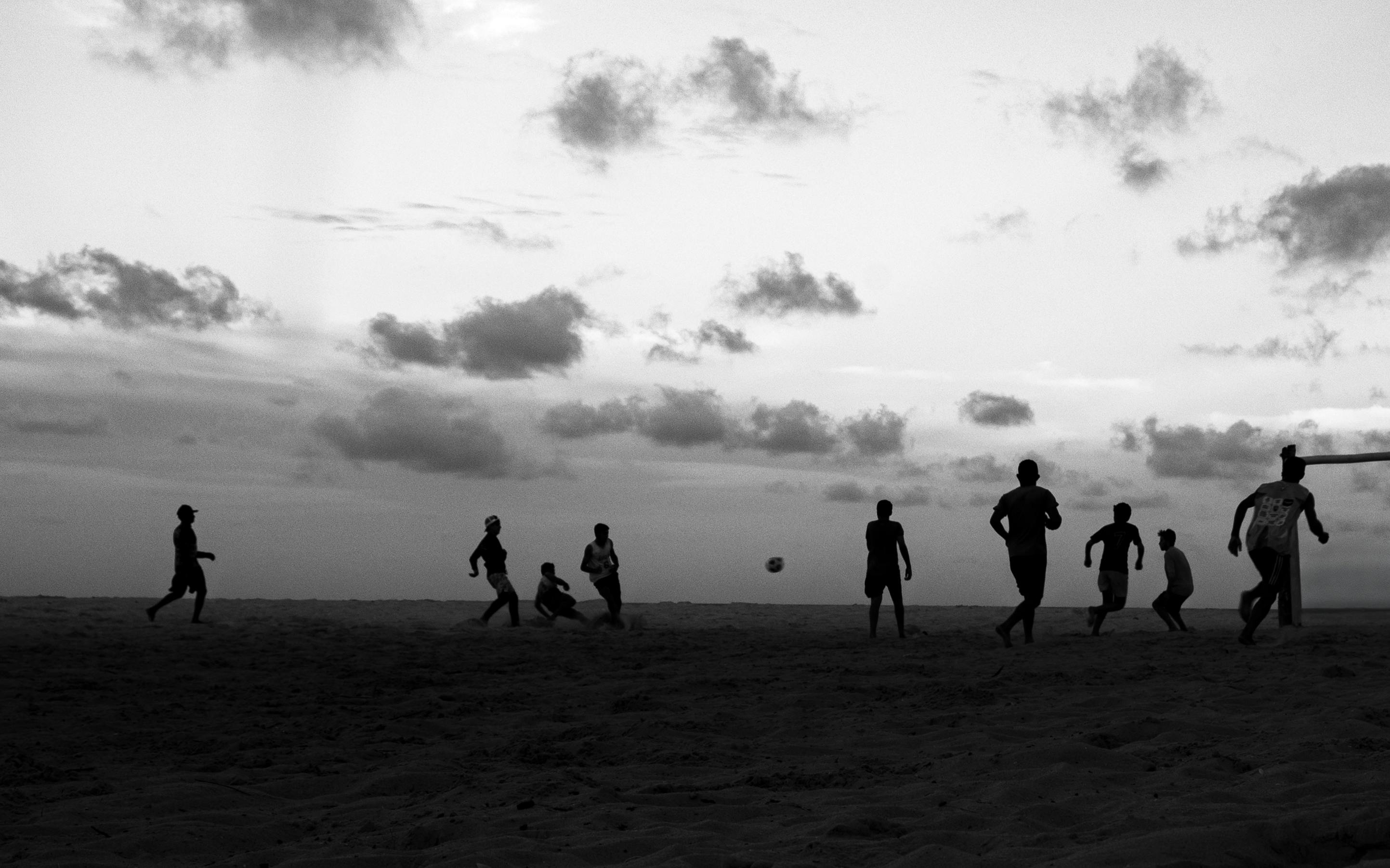 無料 ブラジルのナタールにある砂浜で、夕暮れ時、シルエットになった子供たちがサッカーをしている。 写真素材