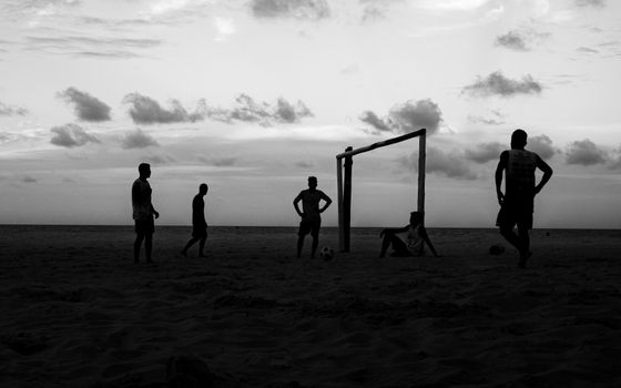 Silhouetted group playing soccer on a beach at sunset in Natal, Brazil.