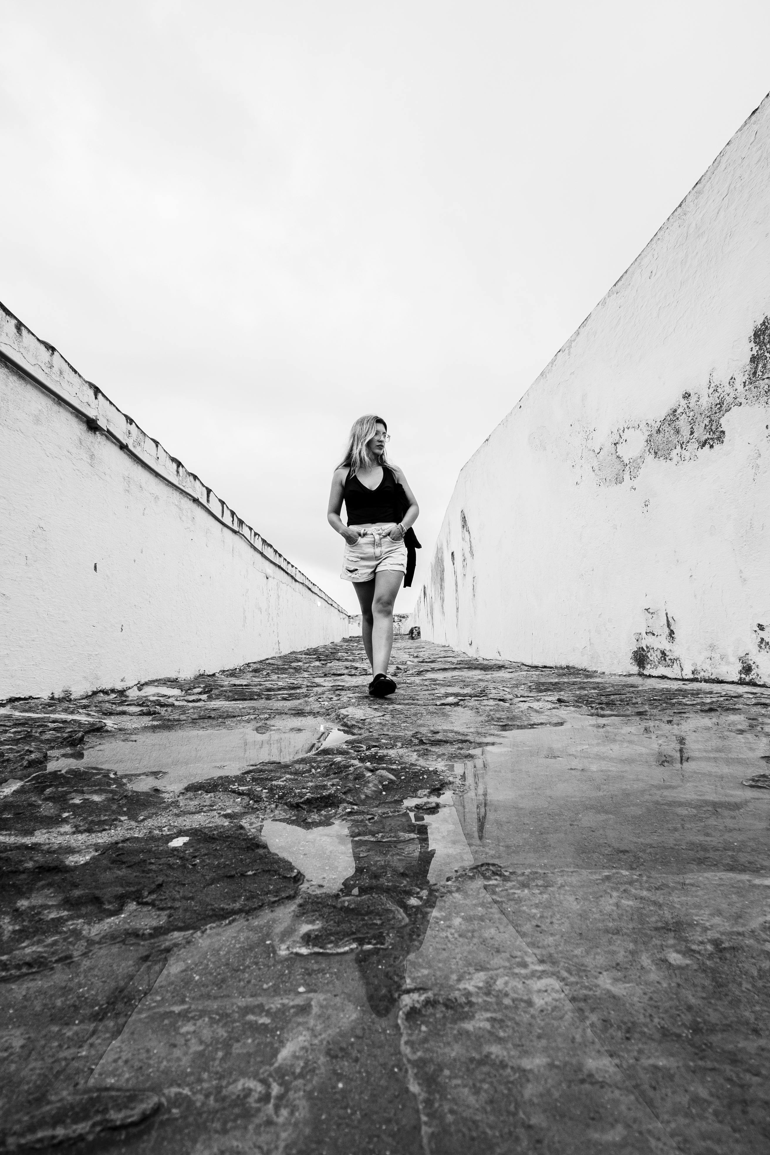 Kostenlos Schwarz-Weiß-Fotografie einer Frau, die auf einem Kopfsteinpflasterweg in Natal, Brasilien, geht, aufgenommen im minimalistischen Stil. Stock-Foto