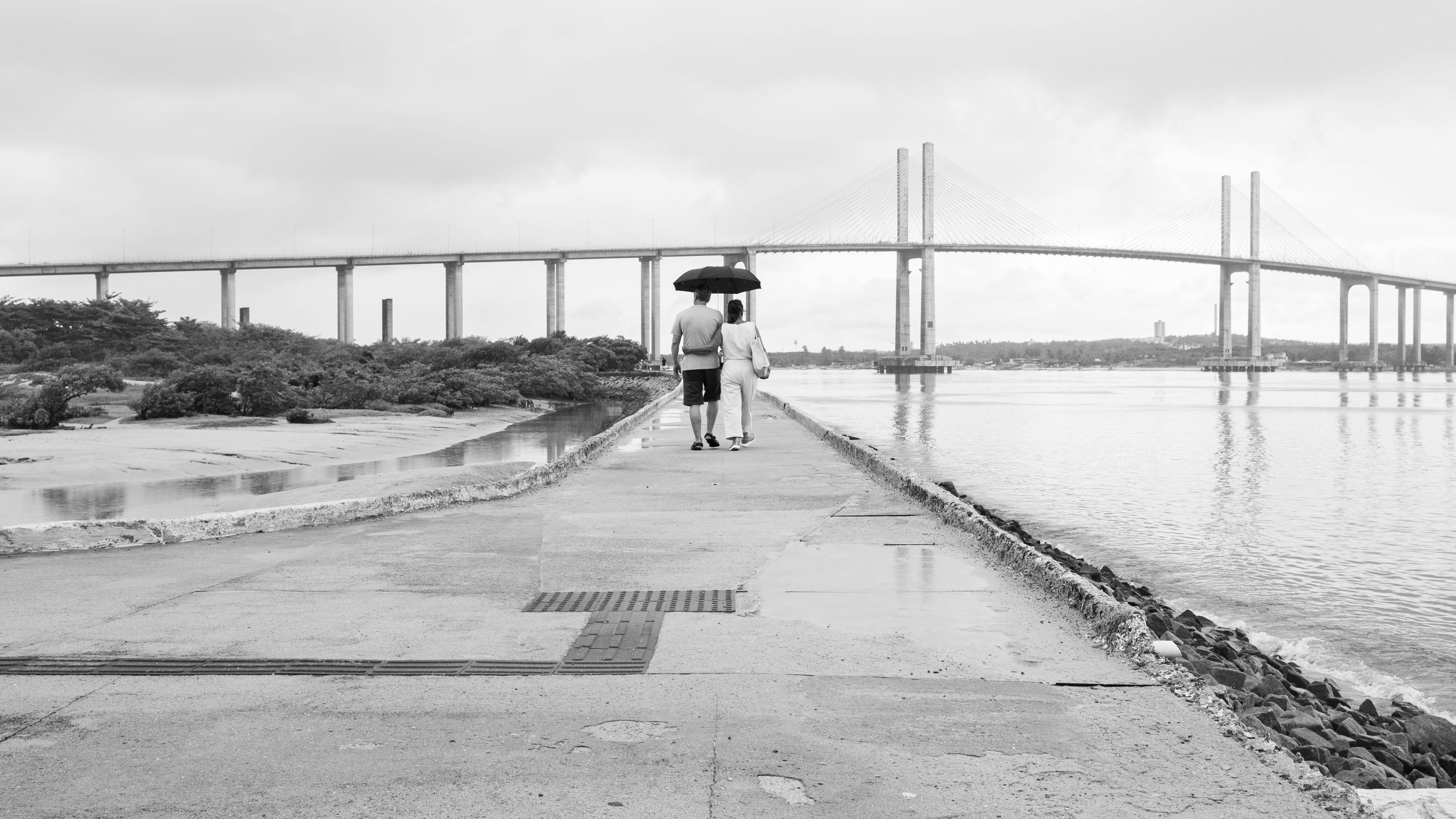 Gratuit Un cuplu cu o umbrelă merge spre un pod din Natal, Brazilia, într-o zi ploioasă. Fotografie de stoc