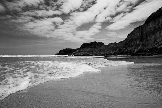 Black and white coastal scene at Natal, Brazil with ocean waves and rocky cliffs.