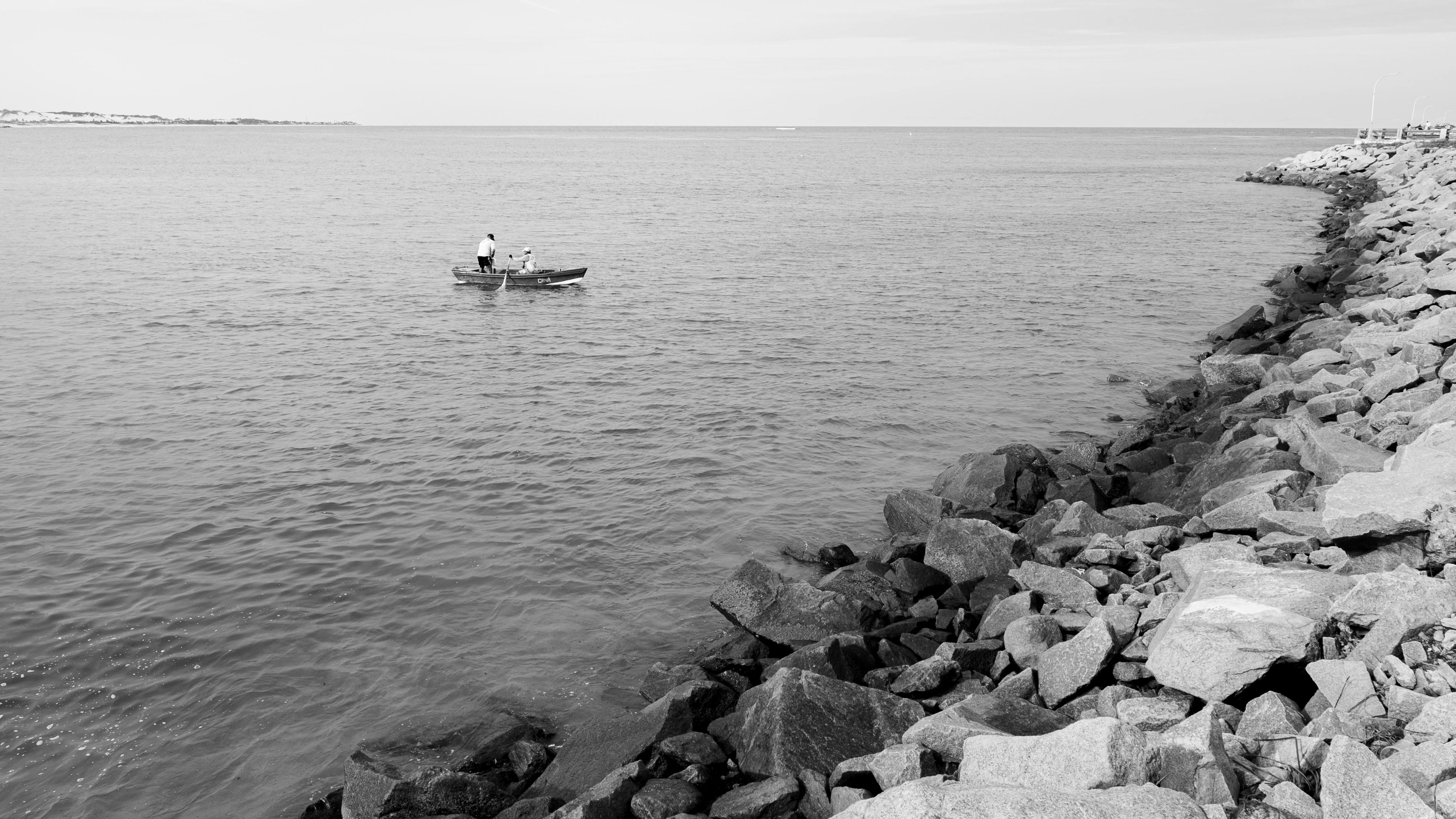 De franc Una serena escena en blanc i negre de dos homes pescant des d'una barca davant la costa rocosa de Natal, Brasil. Foto d'estoc