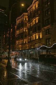 Wet city night shot with car headlights reflecting on rain-soaked streets of New York.