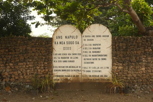 Stone tablet inscribed with religious text, set against a rustic wall in Central Visayas, Philippines.