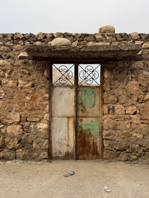 Free Rustic stone wall featuring a weathered metal door, displaying vintage charm and rural architecture. Stock Photo