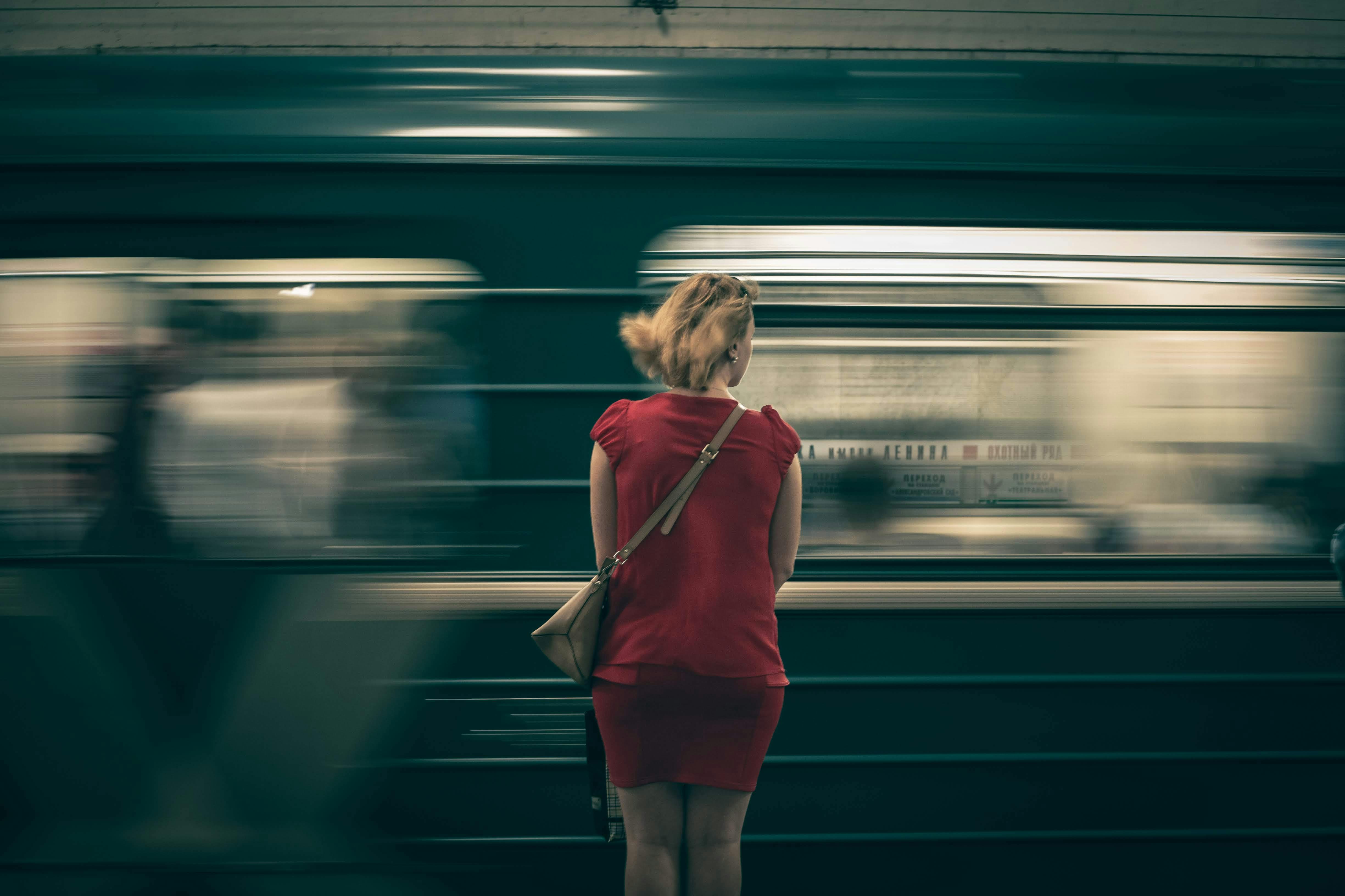 Δωρεάν Μια γυναίκα με κόκκινο φόρεμα περιμένει καθώς ένα τρένο του μετρό περνάει με ταχύτητα θολή, δημιουργώντας μια αίσθηση κίνησης. Φωτογραφία από στοκ φωτογραφιών