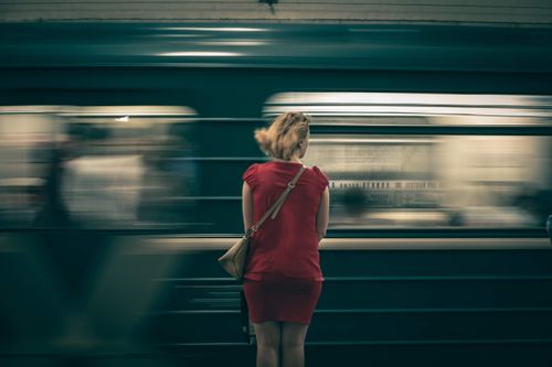Free A woman in a red dress waits as a subway train speeds by in a blur, creating a sense of motion. Stock Photo