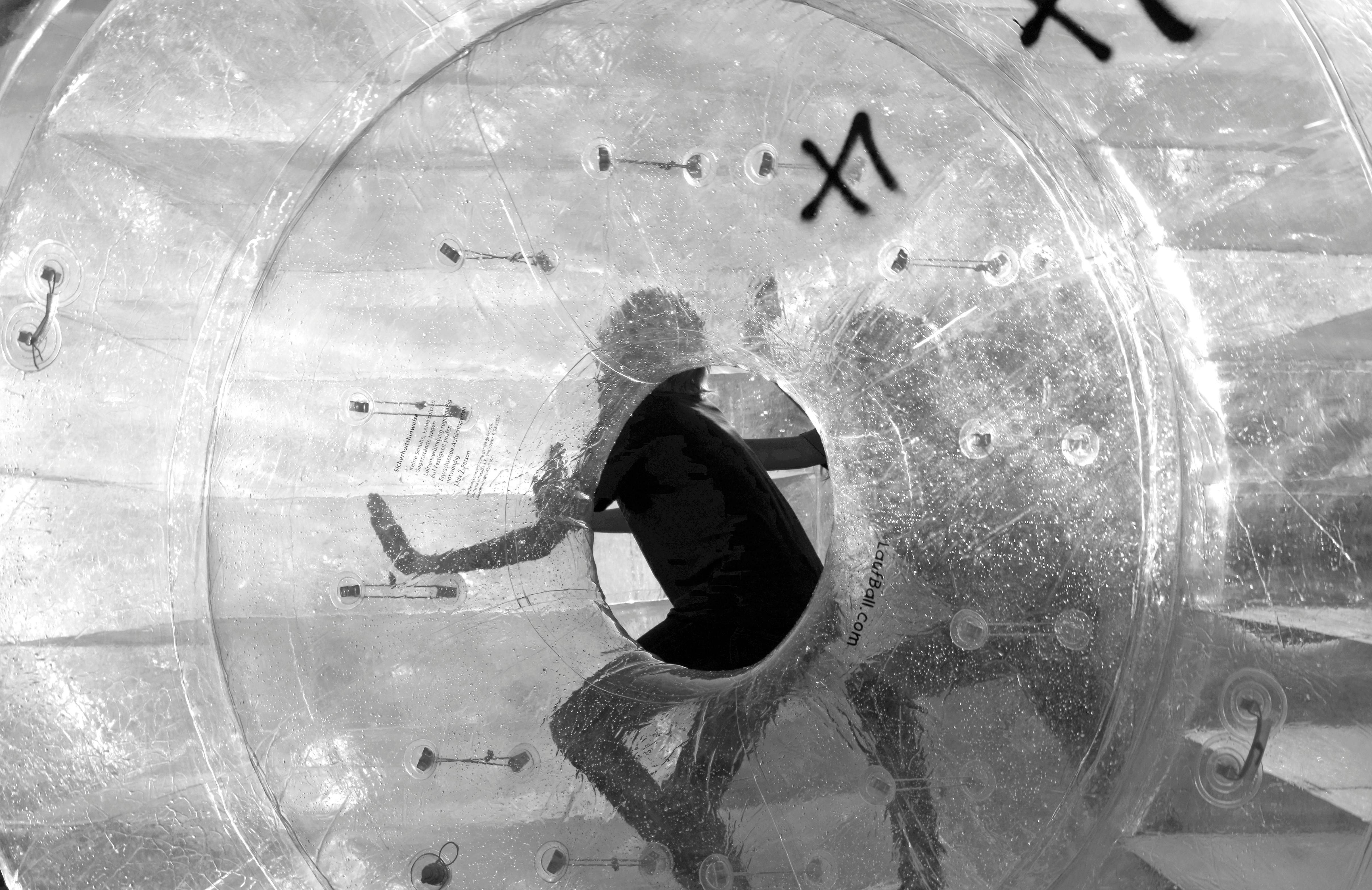 Gratis Imagen en blanco y negro de una persona dentro de una bola de zorbing transparente, creando un efecto de silueta dinámico. Foto de stock