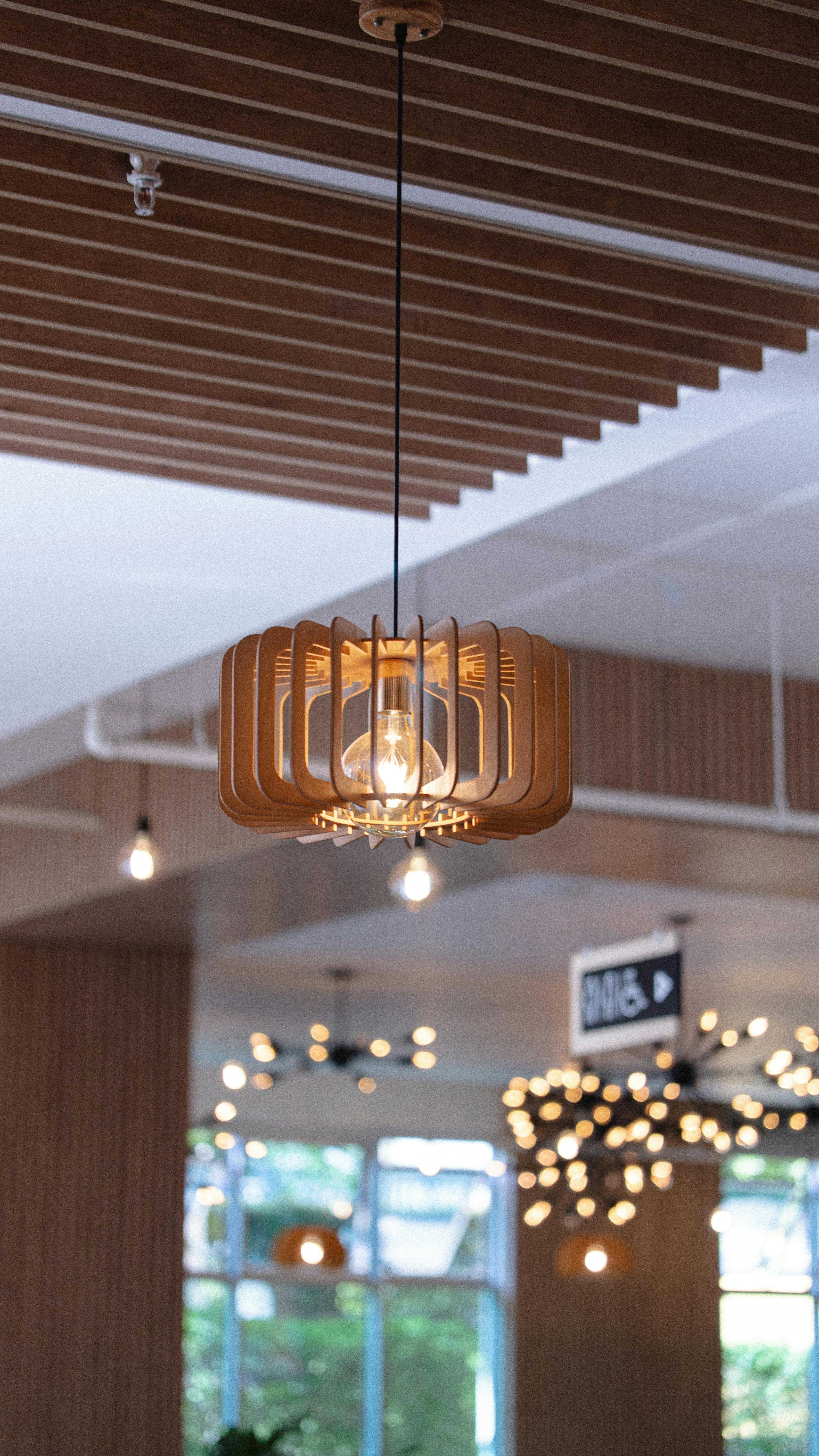A contemporary wooden pendant lamp hangs in a chic indoor cafe setting.