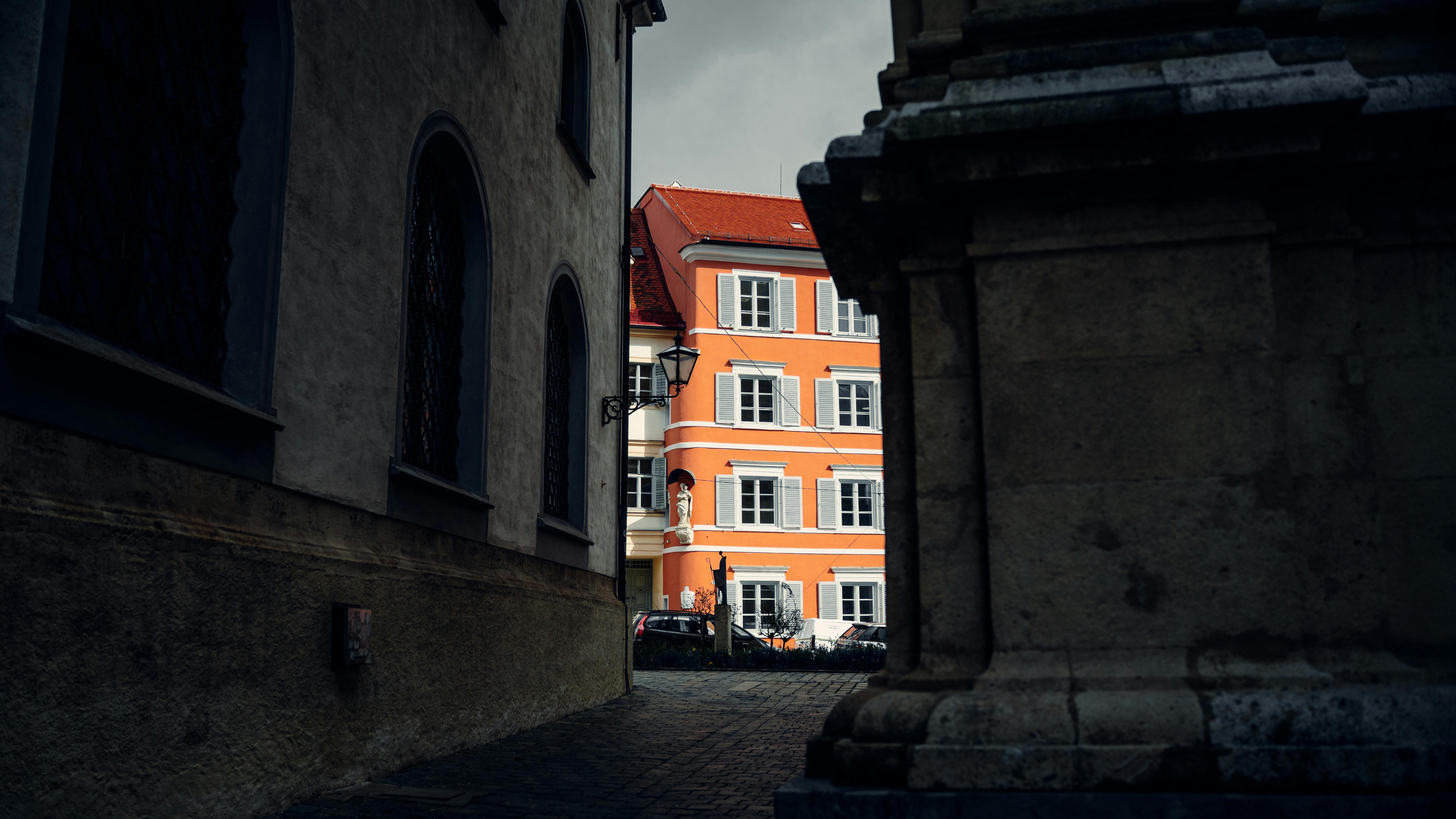 Gratuit O clădire portocalie strălucitoare iese în evidență într-o alee europeană umbroasă, creând un contrast vibrant. Fotografie de stoc
