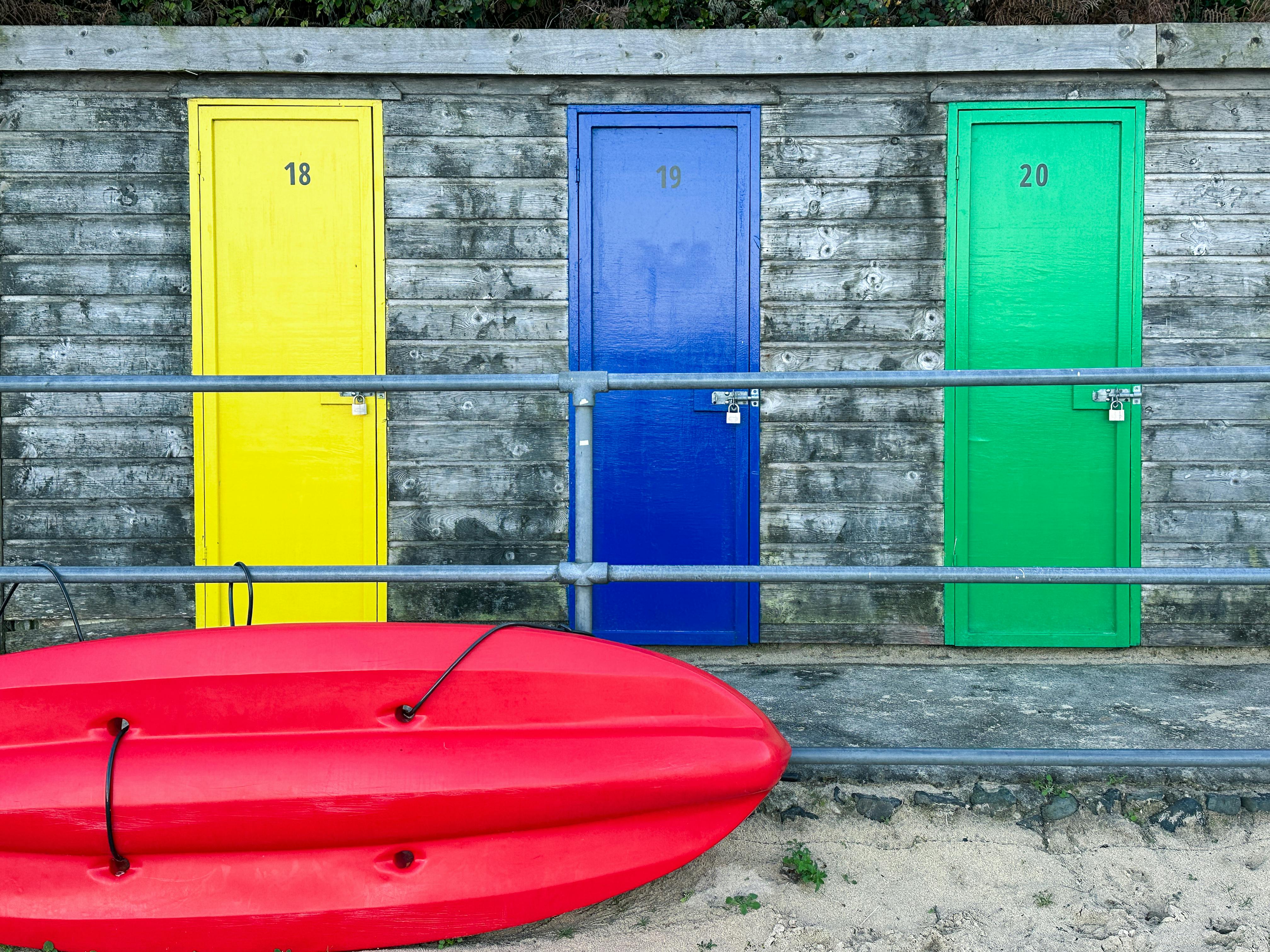 Gratuit Dulapuri de plajă vii cu un caiac roșu la St Ives, Anglia, surprinzând vibrațiile vibrante ale verii. Fotografie de stoc