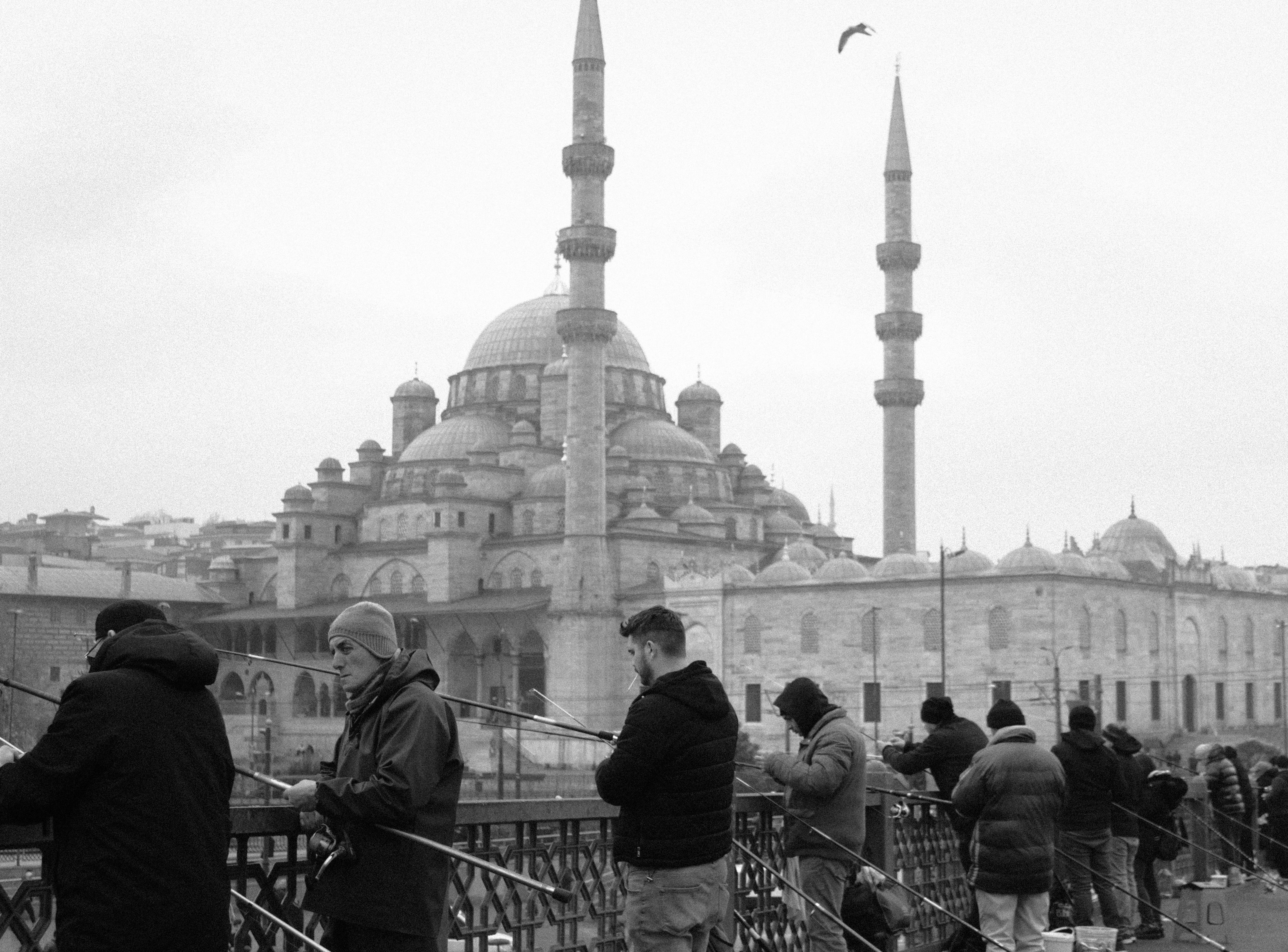 無料 イスタンブールのガラタ橋に立つ漁師たち。背景には新モスクがそびえ立ち、活気あふれる都市の風景が広がっている。 写真素材