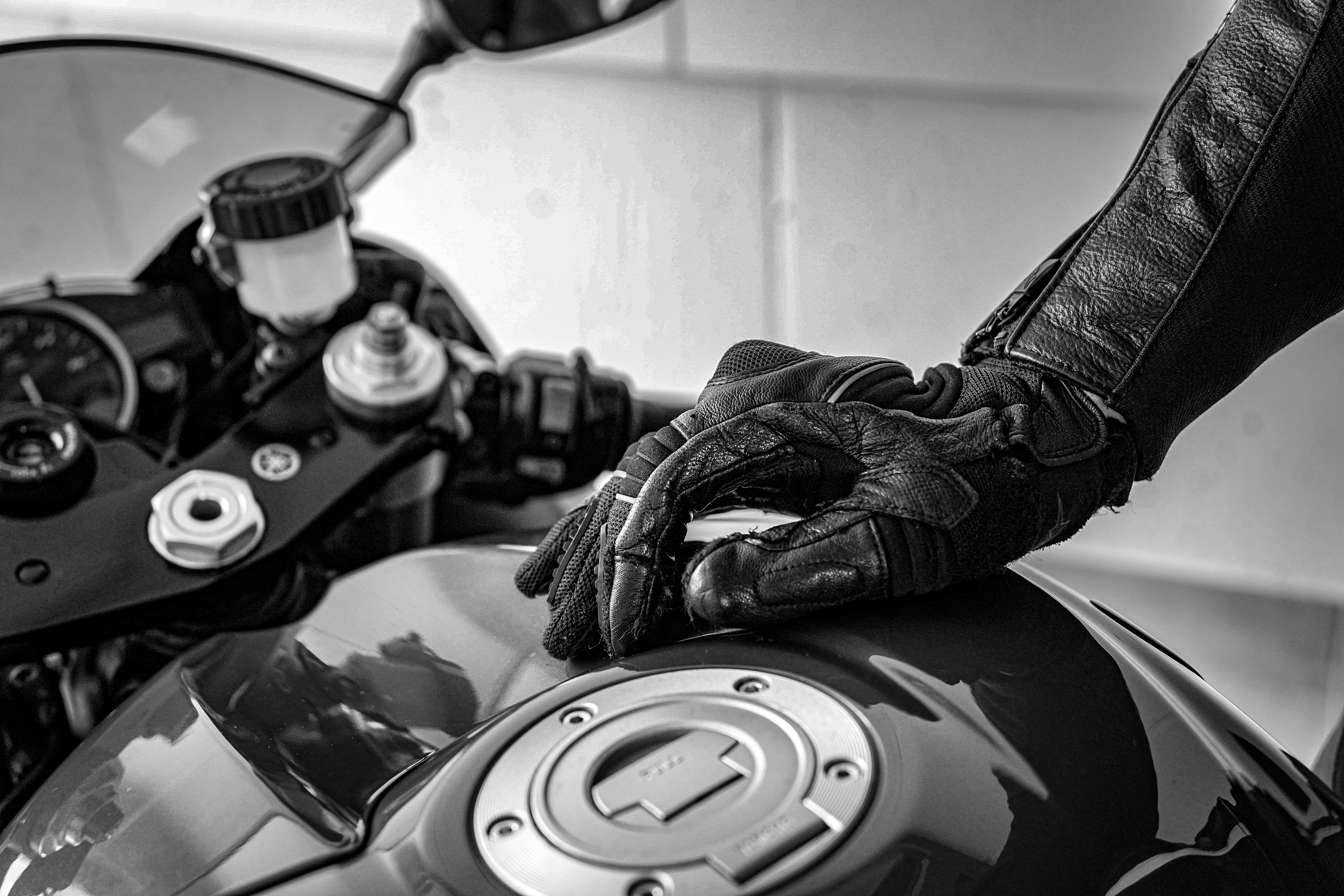 Free Artistic black and white shot of a motorcycle with a gloved hand on the fuel tank, emphasizing textures. Stock Photo
