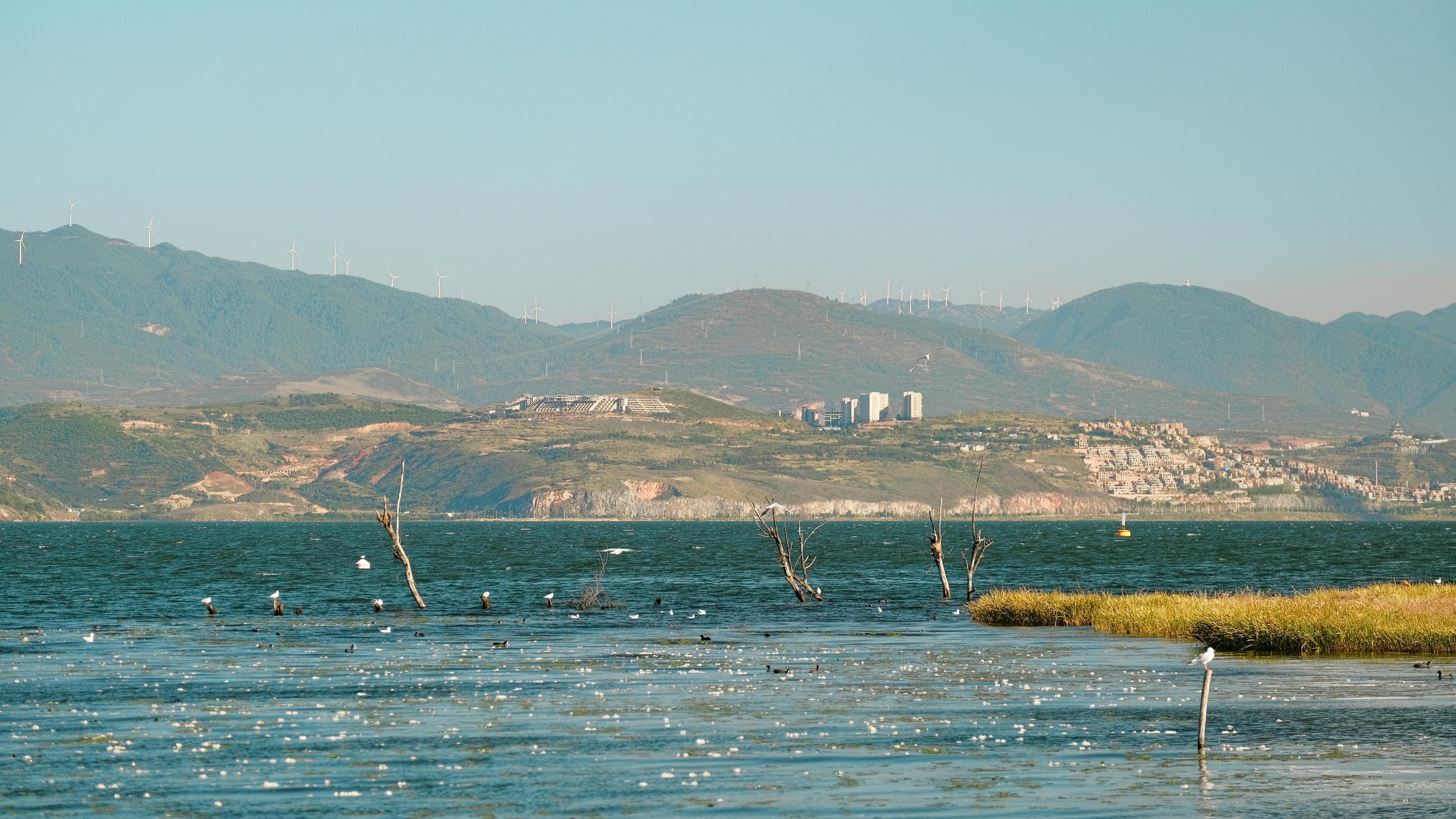 無料 中国大理白族自治州の洱海湖の穏やかな風景。遠くには山々と風力タービンが見える。 写真素材