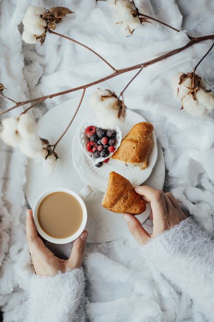 Top view of a cozy breakfast setup with croissants, berries, and coffee surrounded by cotton branches.