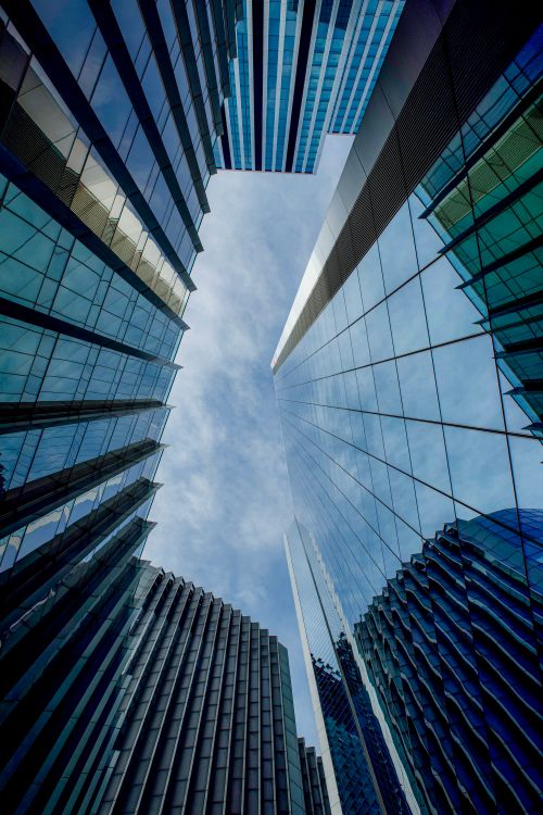 Free Capture of towering modern skyscrapers converging towards the sky, reflecting the clouds. Stock Photo