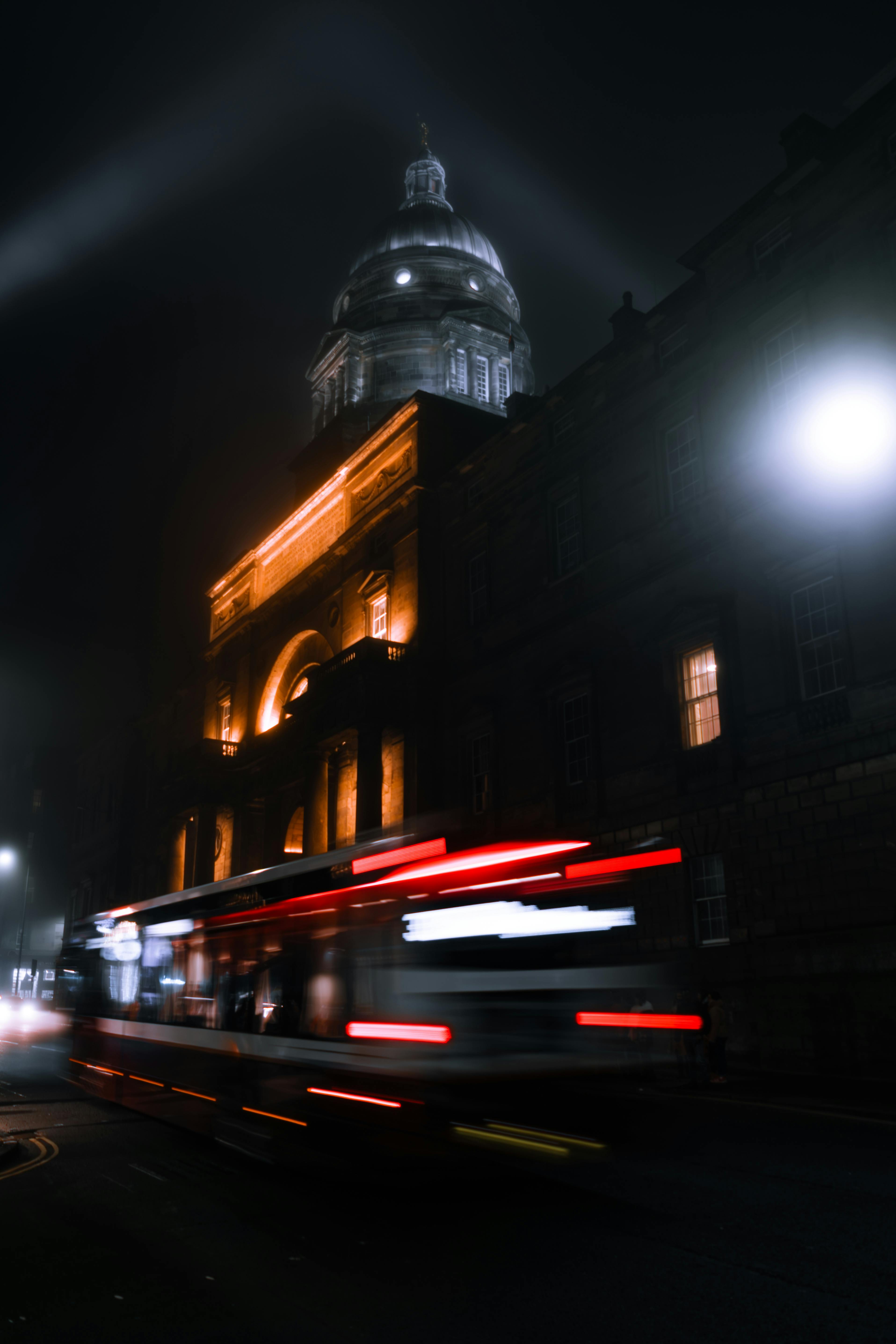 Kostenlos Ein historisches Gebäude, nachts beleuchtet, während der Verkehrslärm eine dynamische Szene erzeugt. Stock-Foto