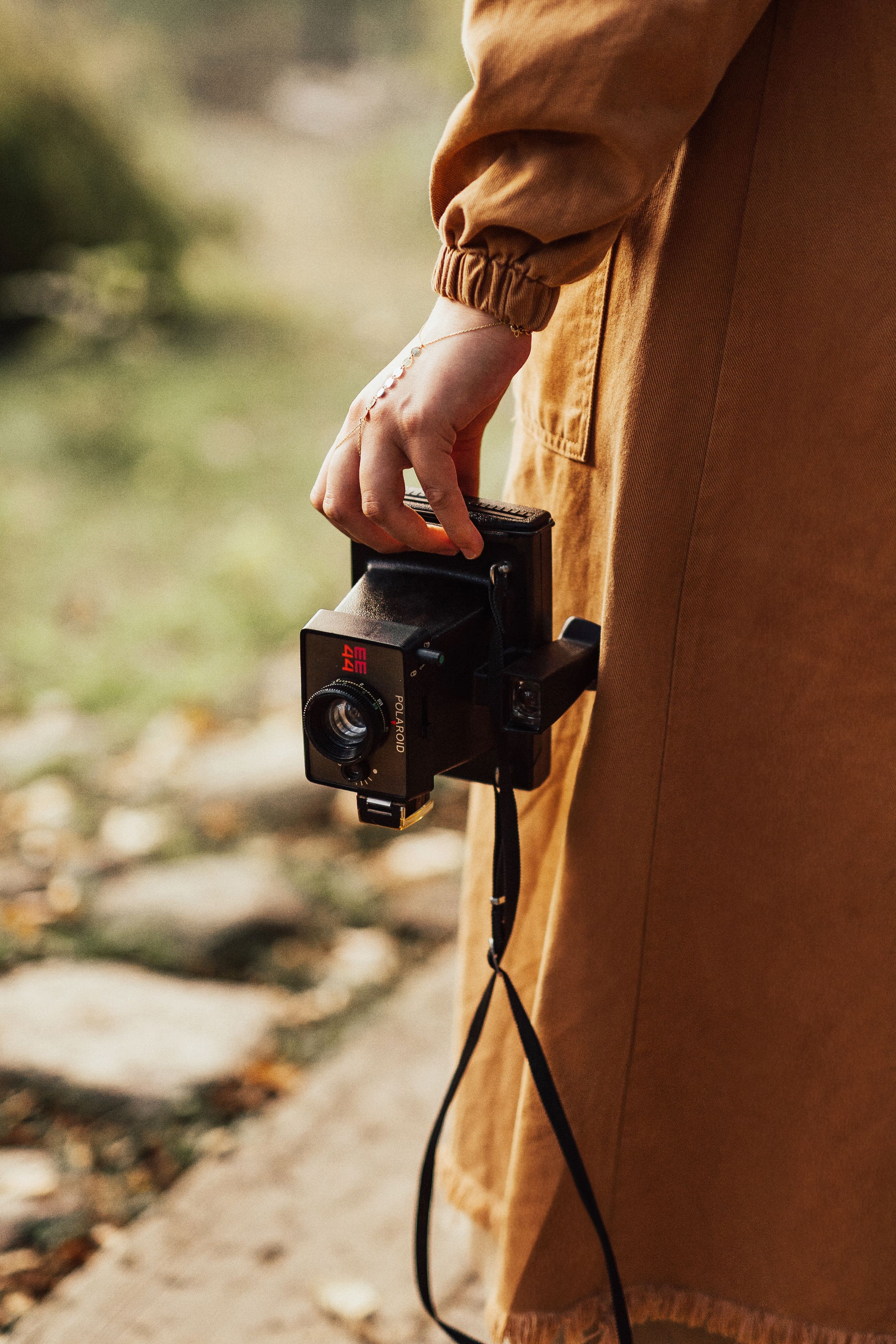 Close-up of a person holding a vintage Polaroid camera outdoors in autumn.