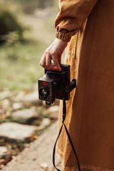 Close-up of a person holding a vintage Polaroid camera outdoors in autumn.