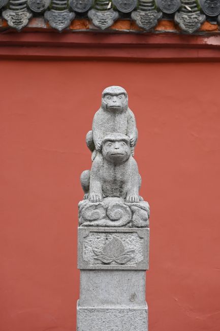 Two stone monkey statues on a pedestal against a traditional red wall.