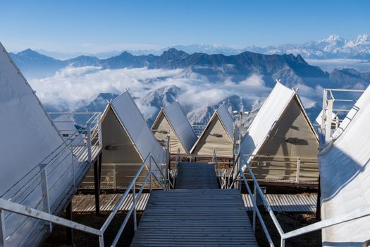 Panoramic view of mountain range with tents, clouds, and clear sky, perfect for adventure lovers.