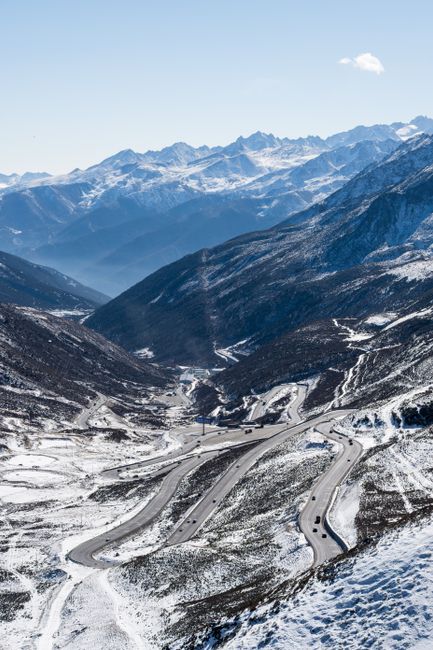 Aerial view of a winding highway through snow-covered mountains under a clear sky.