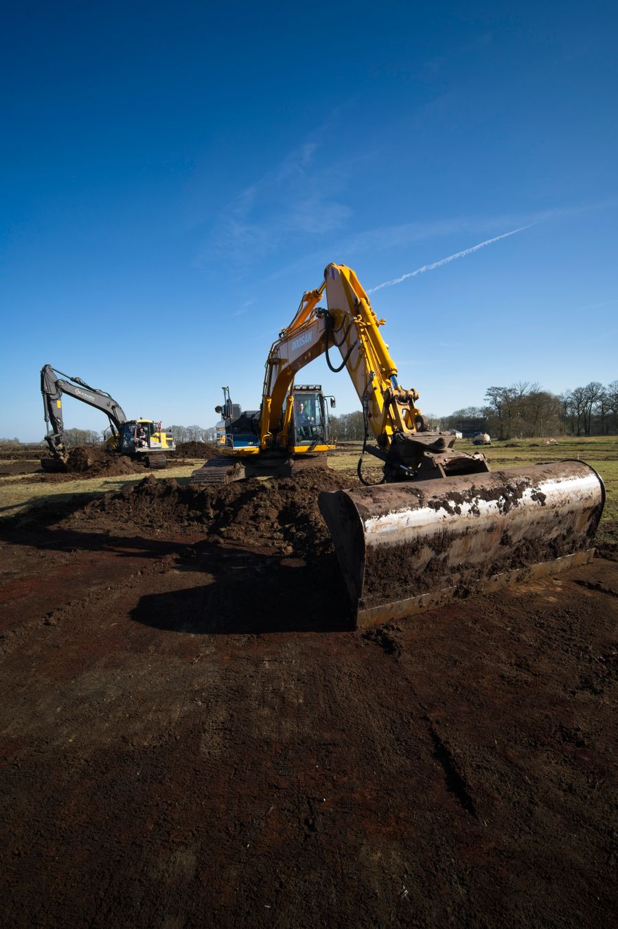 Two excavators working a dirt mound under a blue sky