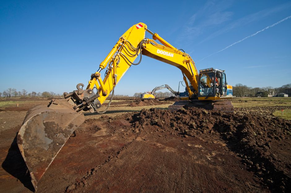 A yellow excavator working on an earthmoving project in the countryside under a clear blue sky.
