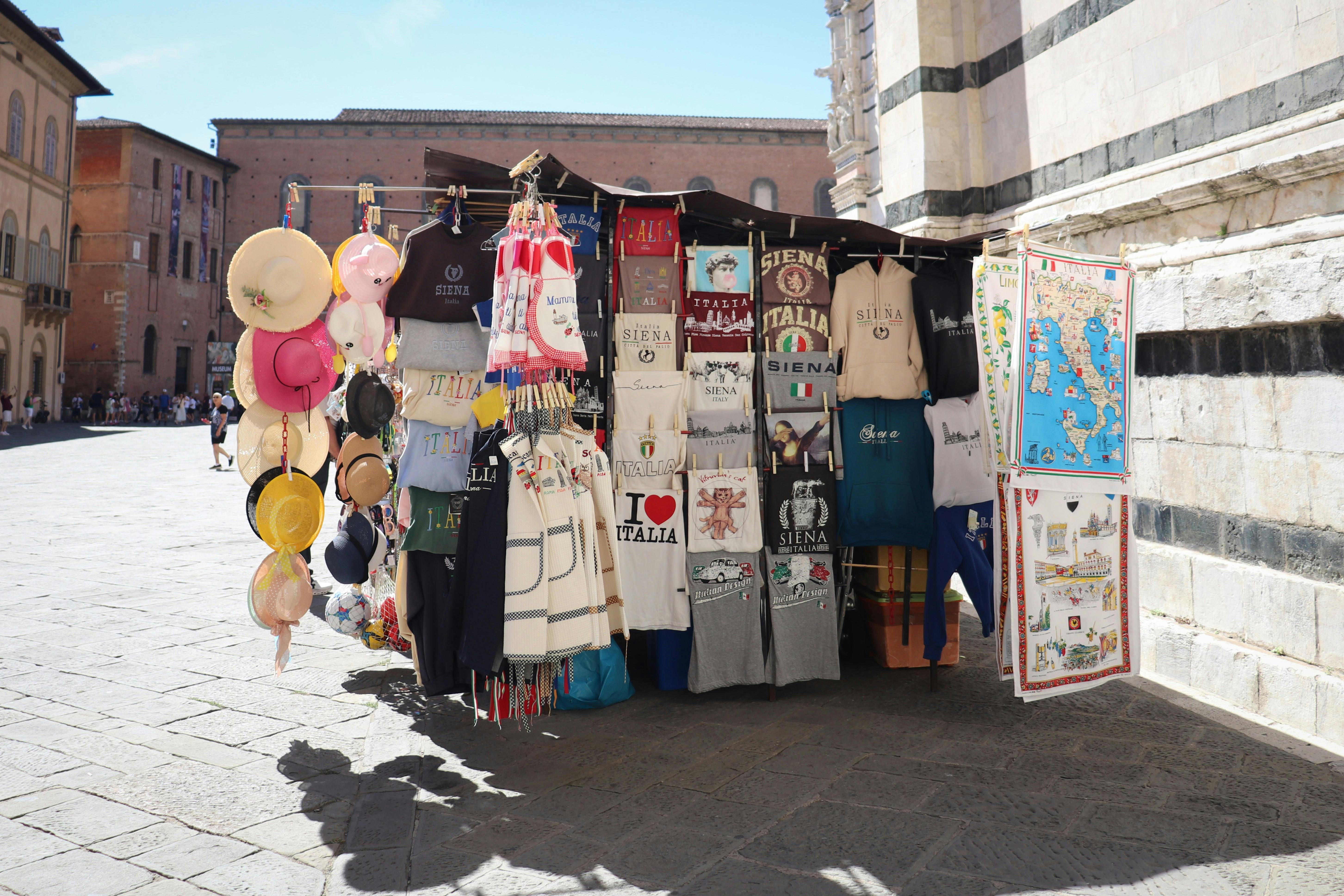 Gratis Affascinante bancarella di souvenir italiani a Siena con cappelli e magliette dai colori vivaci. Foto a disposizione