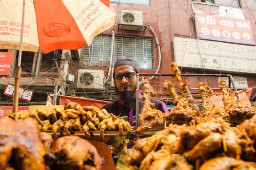 Street food vendor selling grilled chicken in a vibrant Dhaka market.